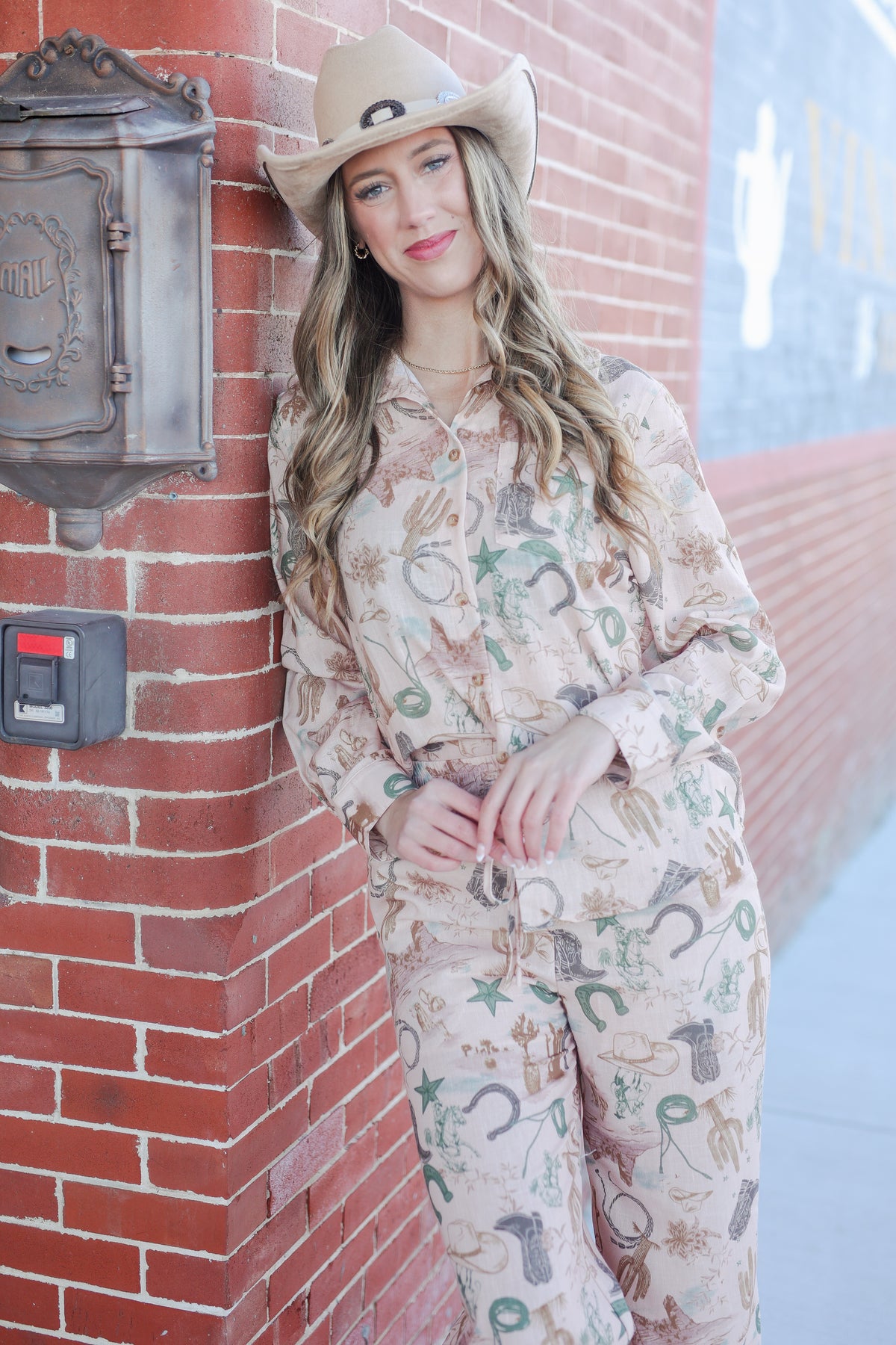 Woman in a patterned outfit leaning against a brick wall.