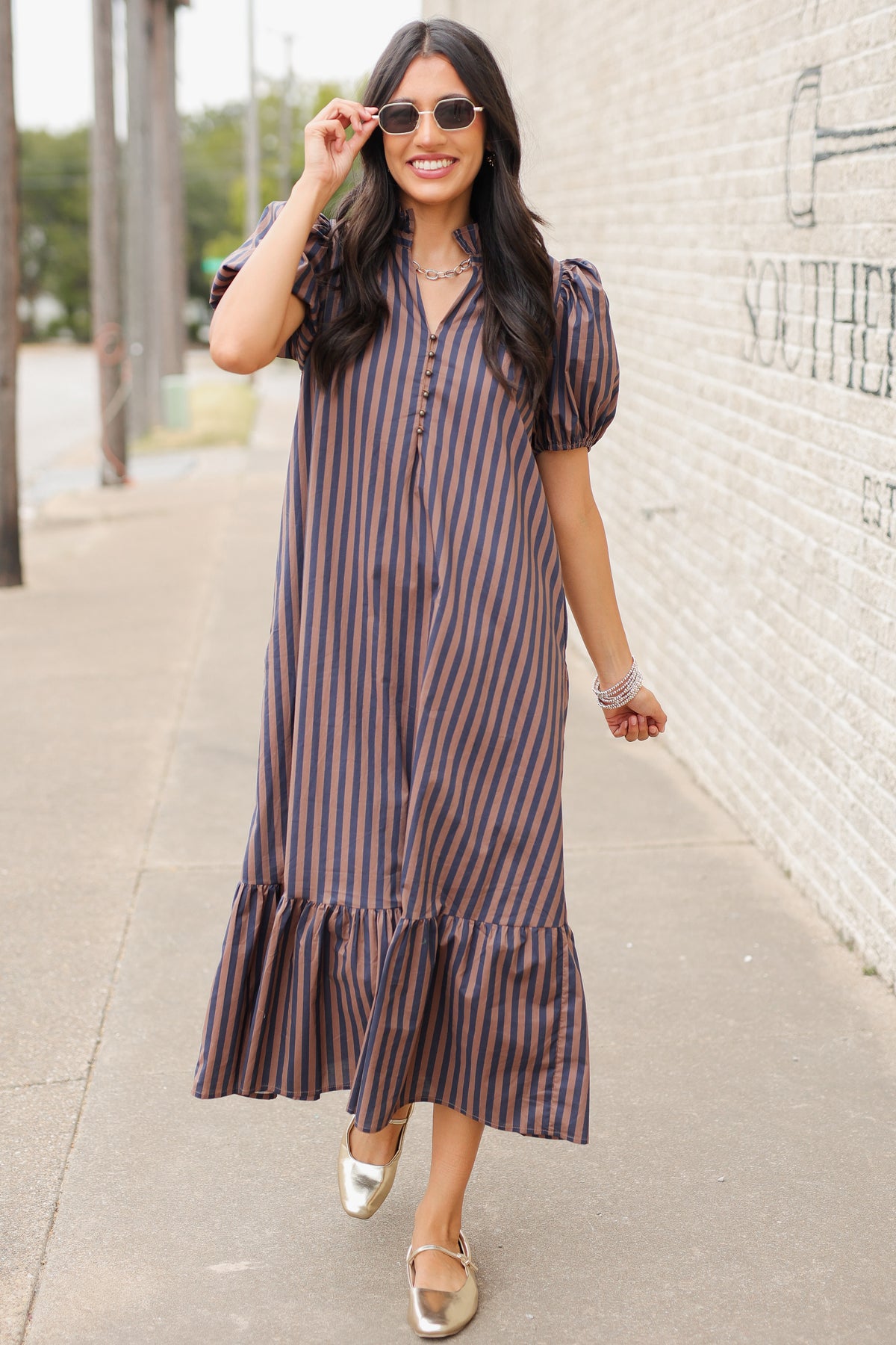 Brunette model wearing a navy and brown dress standing outside. Southern House Clothing