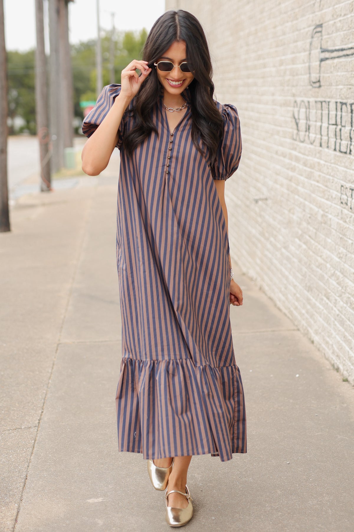 Brunette model wearing a navy and brown dress standing outside. Southern House Clothing