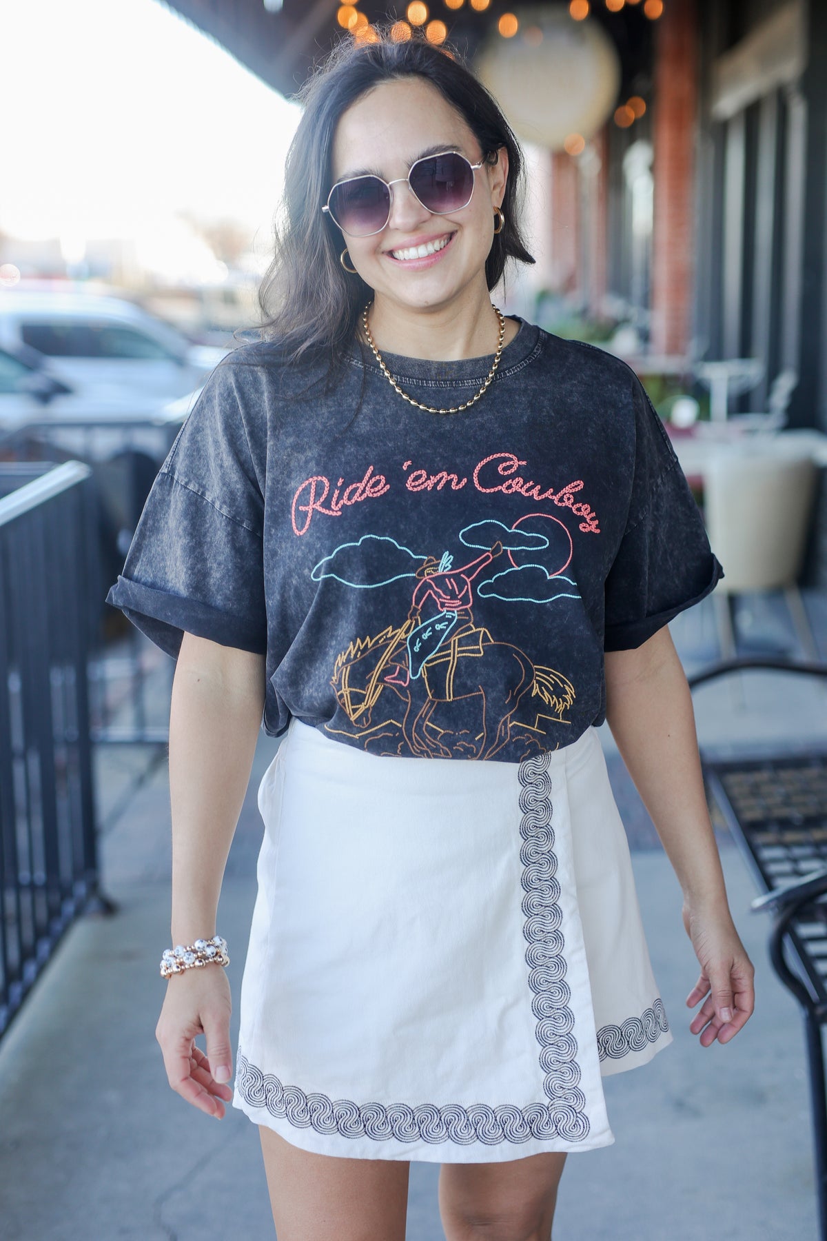 Woman wearing a graphic t-shirt with text and graphics, standing outdoors.