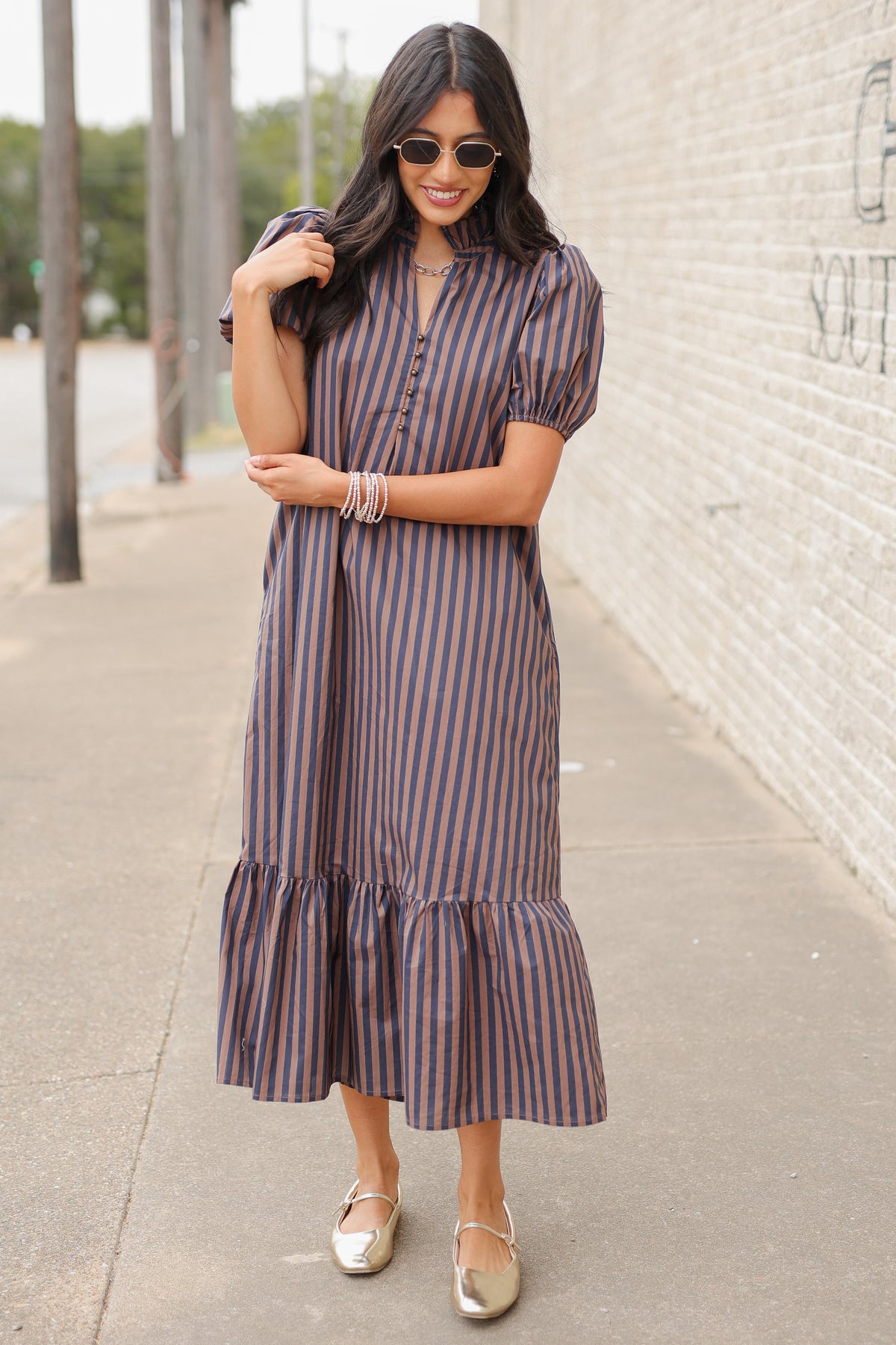 Brunette model wearing a navy and brown dress standing outside. Southern House Clothing