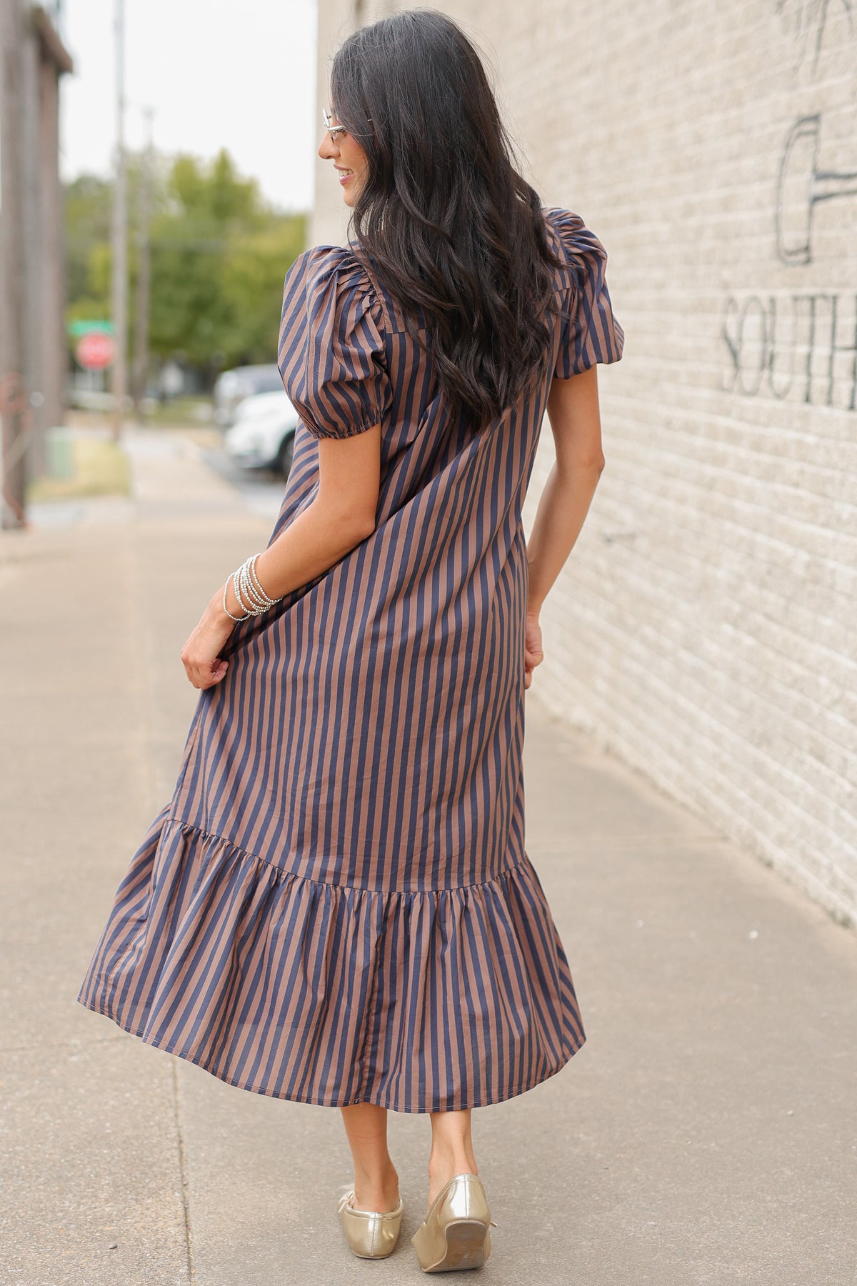 Brunette model wearing a navy and brown dress standing outside. Southern House Clothing