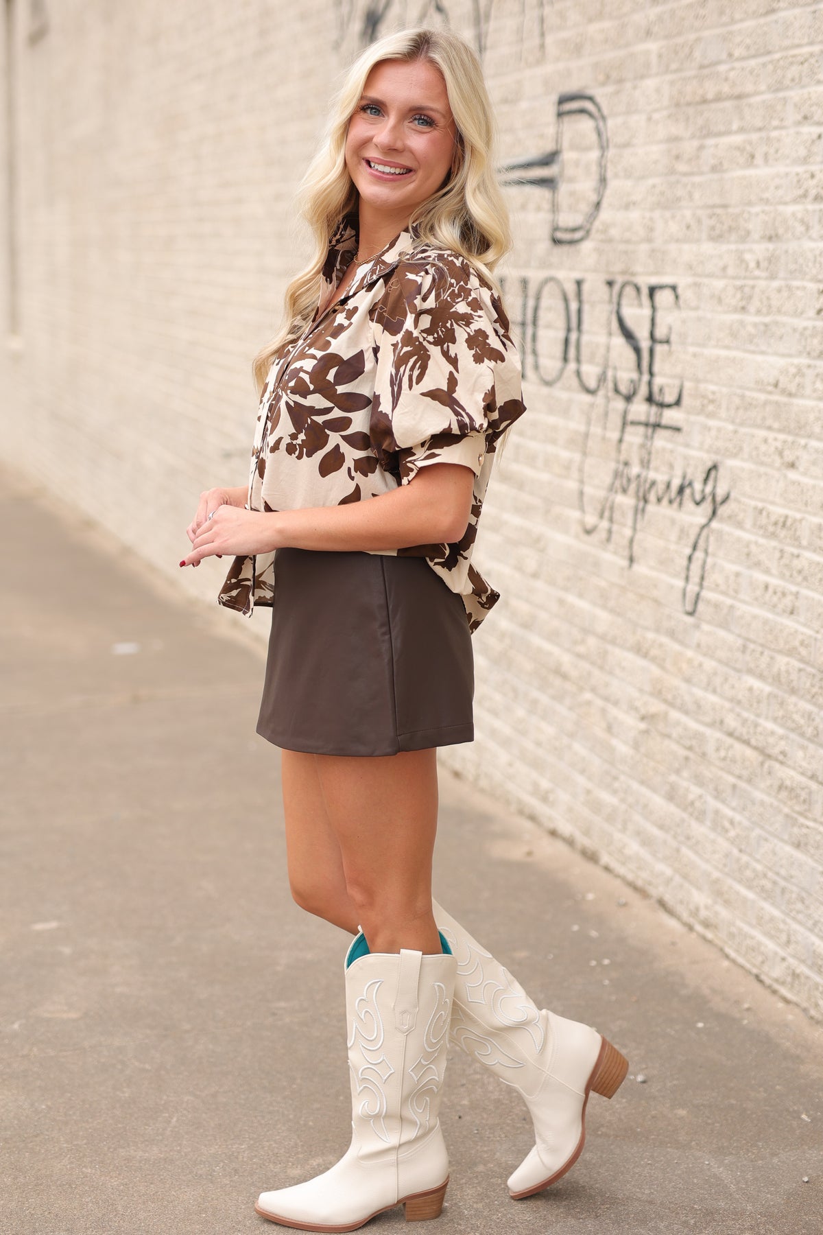 Blonde model wearing the Ainsley top with a brown faux leather skirt and the senora boots in white standing outside. | Southern House Clothing |