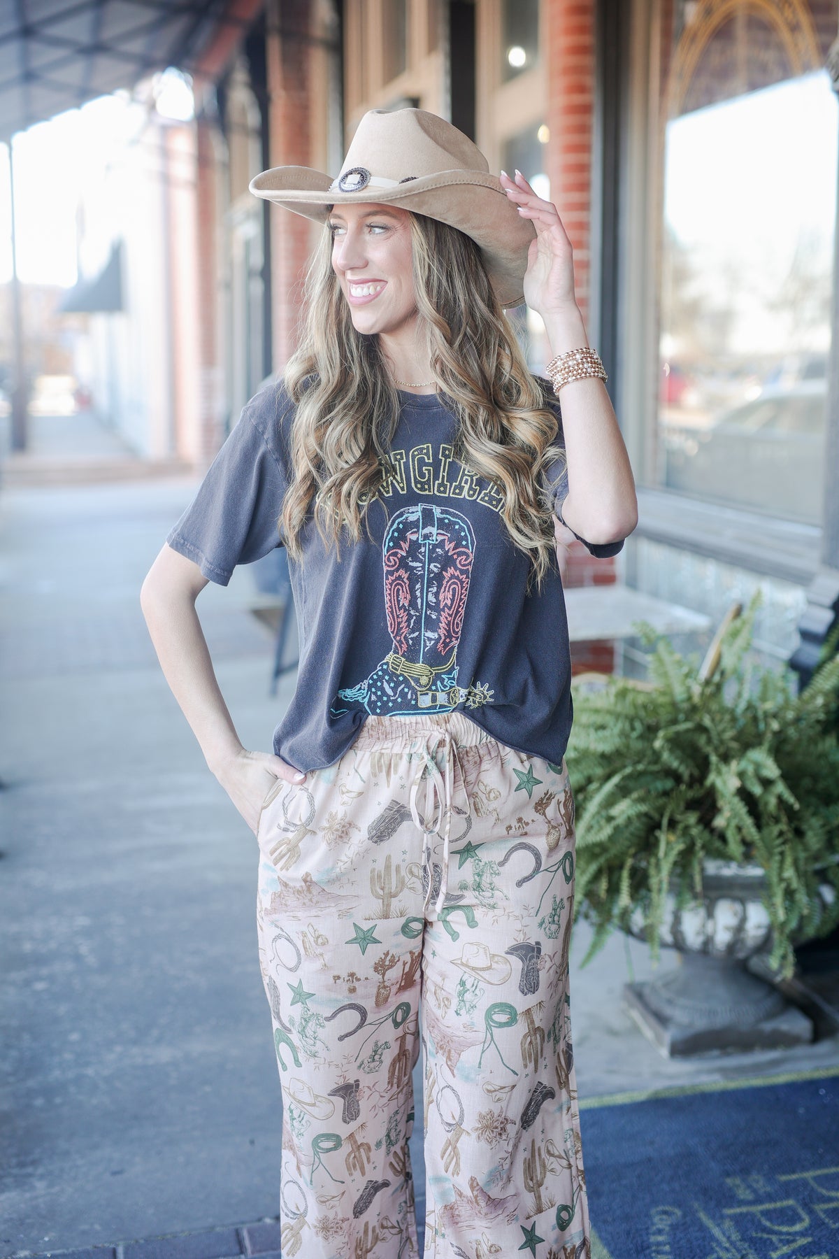 Woman wearing a cowboy hat and graphic t-shirt with patterned pants on a street.