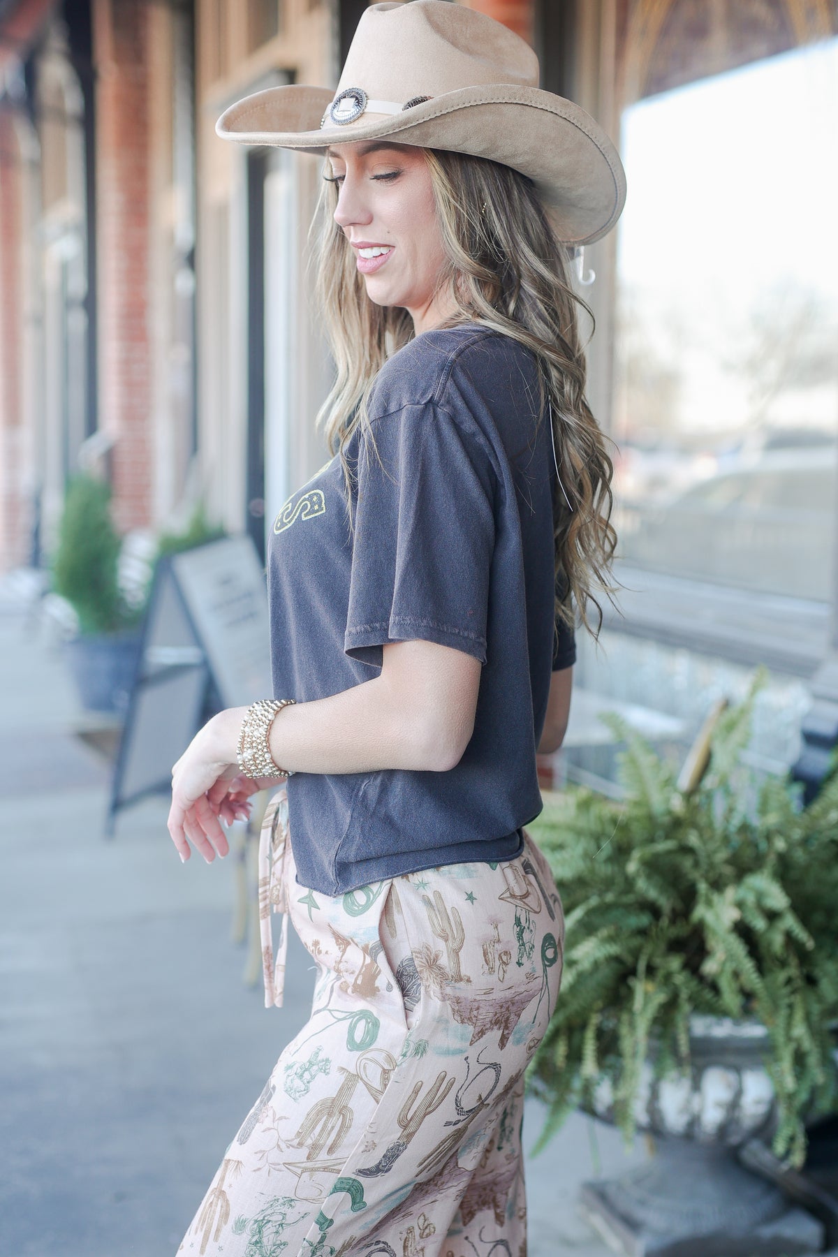 Woman wearing a cowboy hat and casual outfit standing outdoors.