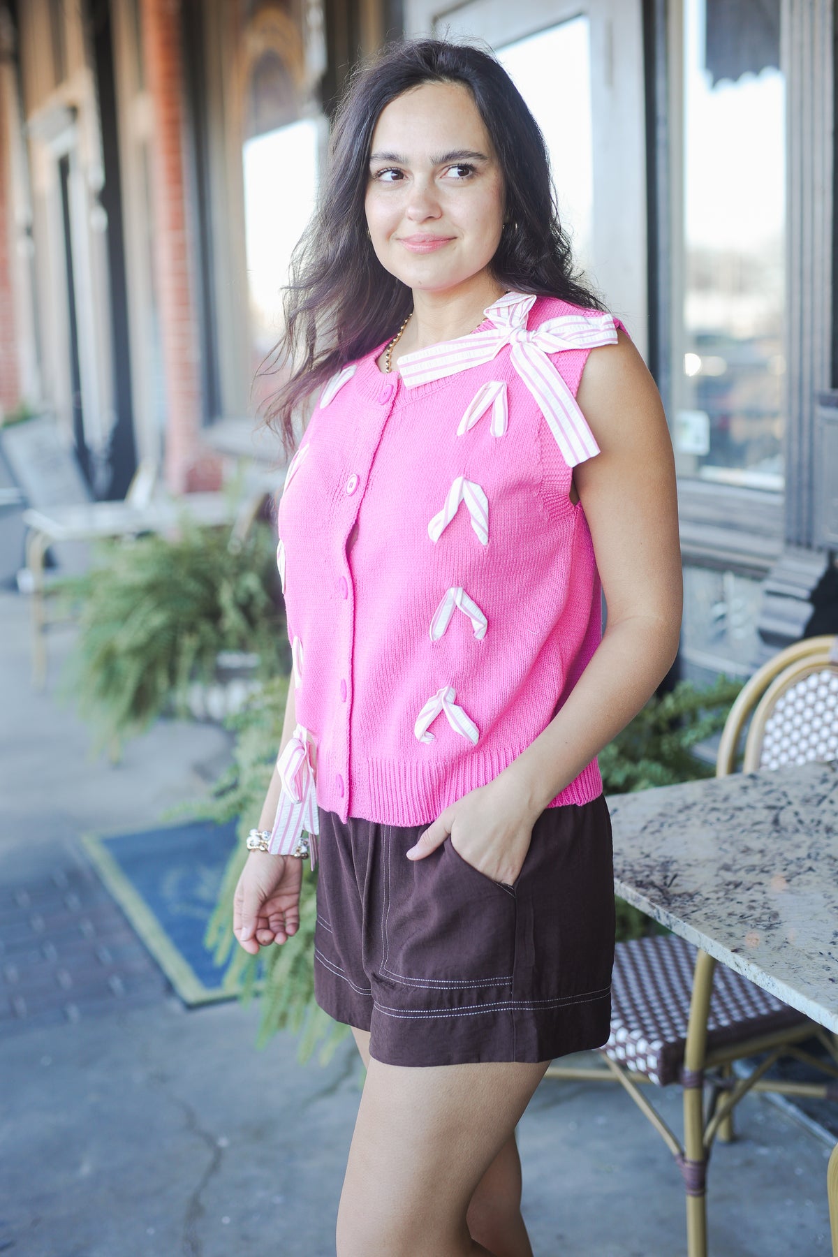 Woman wearing a pink cardigan with white accents outdoors.
