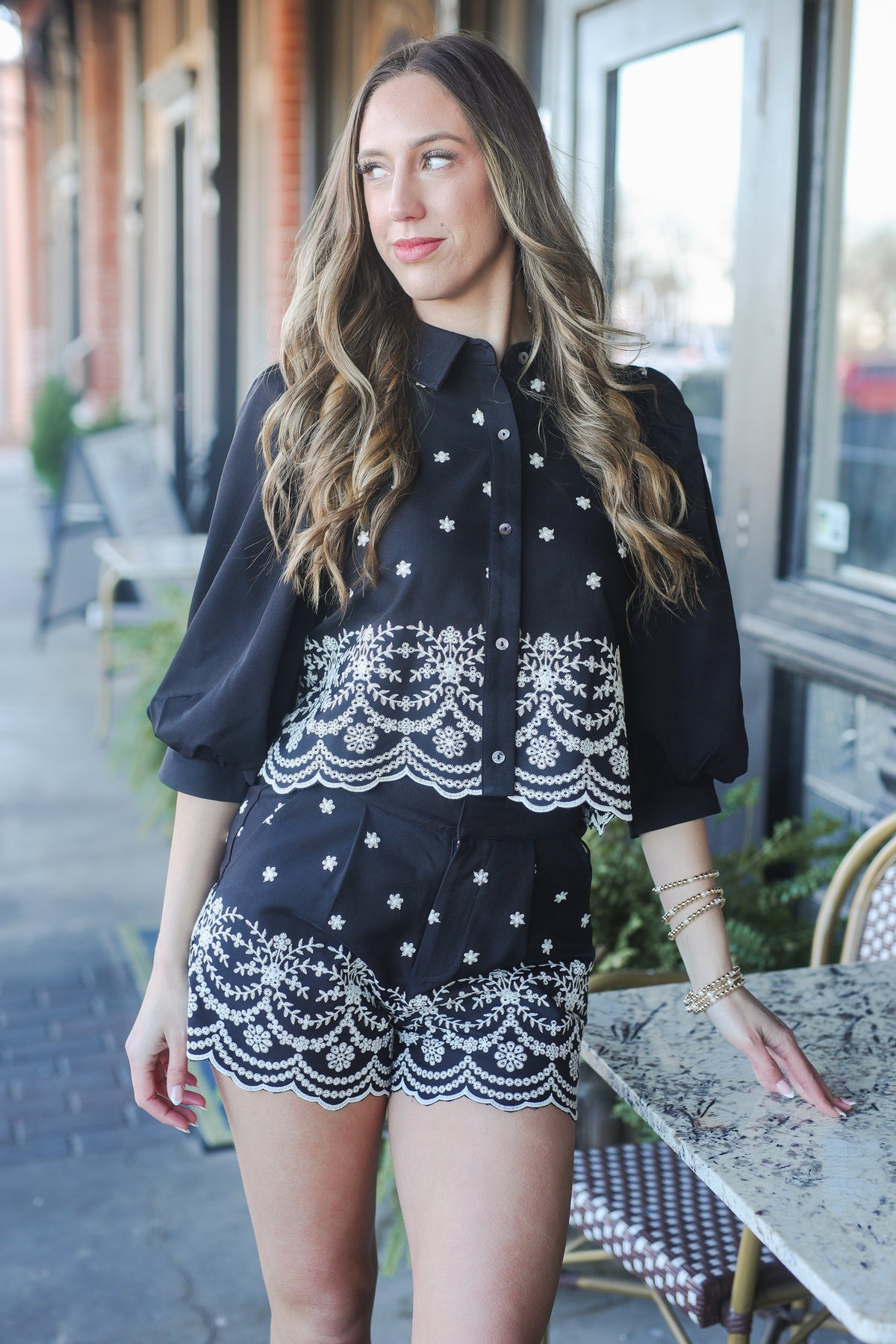 Woman wearing a black blouse with white lace details and matching shorts, standing outdoors.