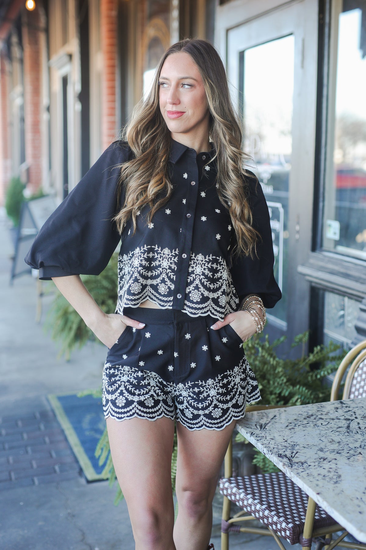 Woman wearing a black blouse with white lace details and matching shorts outdoors.