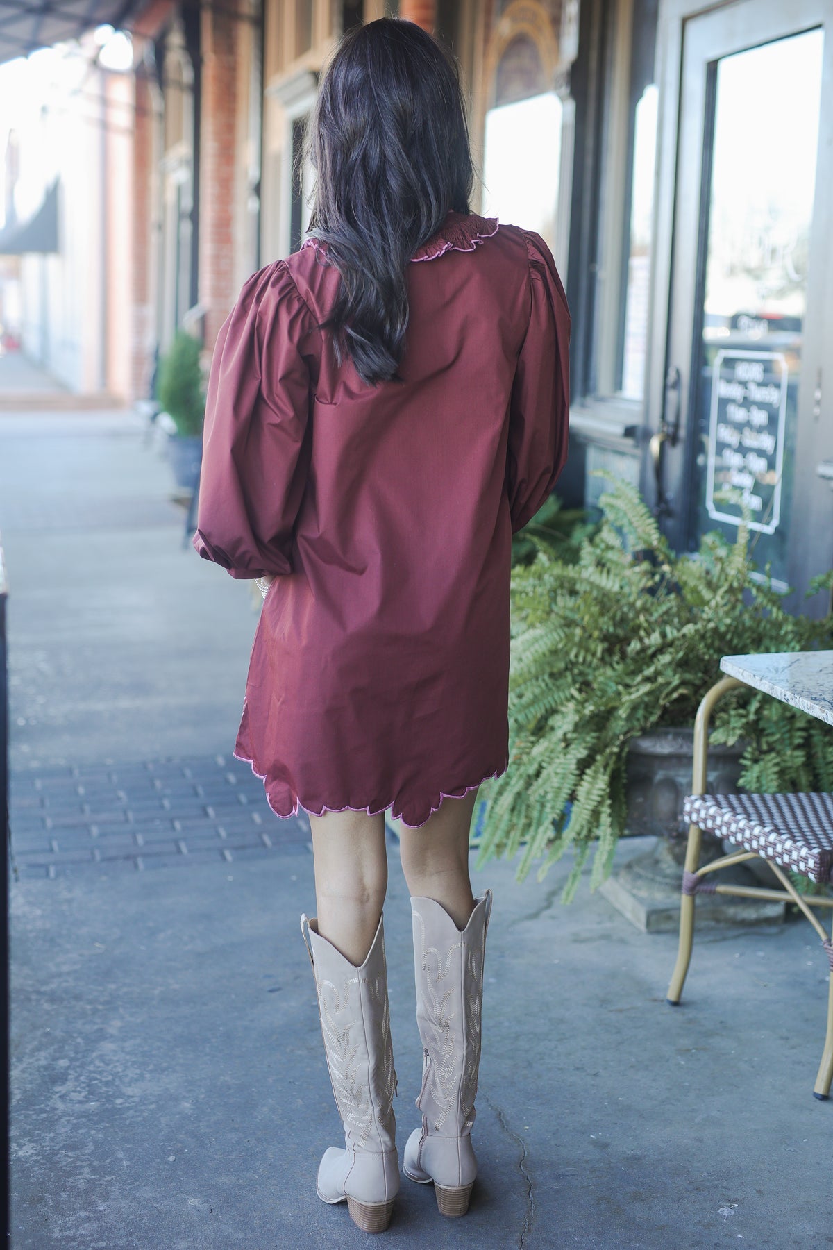 Woman in a burgundy dress and beige knee-high boots walking on a sidewalk.