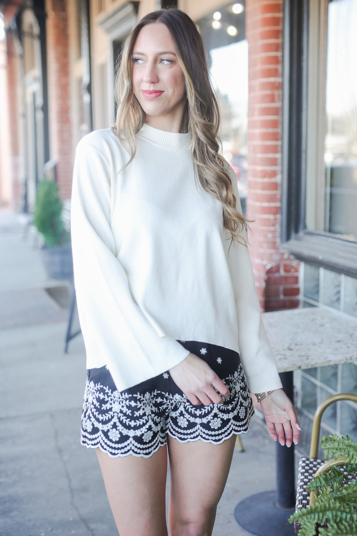 Woman wearing a white sweater and black lace skirt standing outdoors.