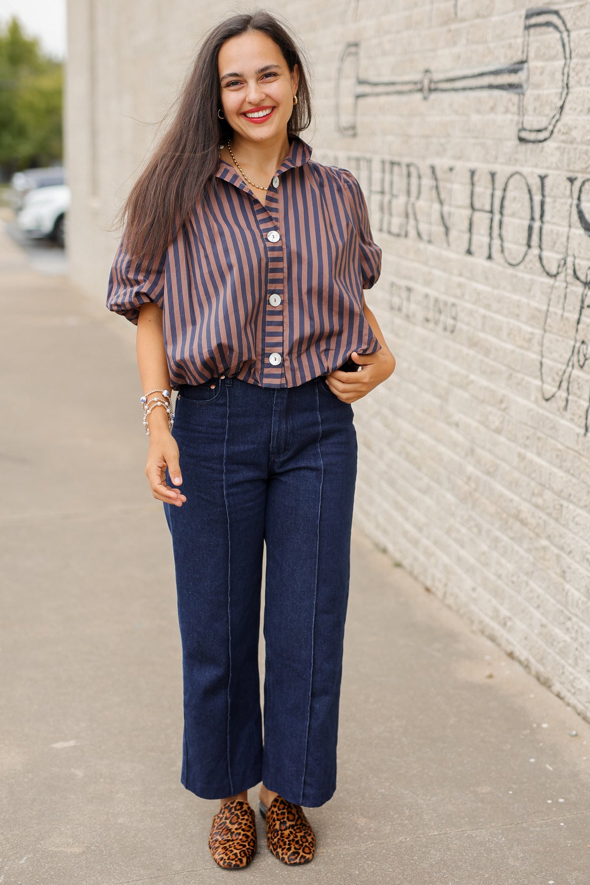 Brunette model wearing a navy and brown stripped bubble top and dark denim jeans outside. Southern House Clothing