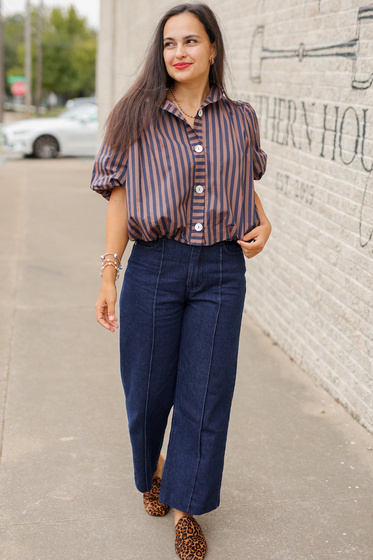 Brunette model wearing a navy and brown stripped bubble top and dark denim jeans outside. Southern House Clothing
