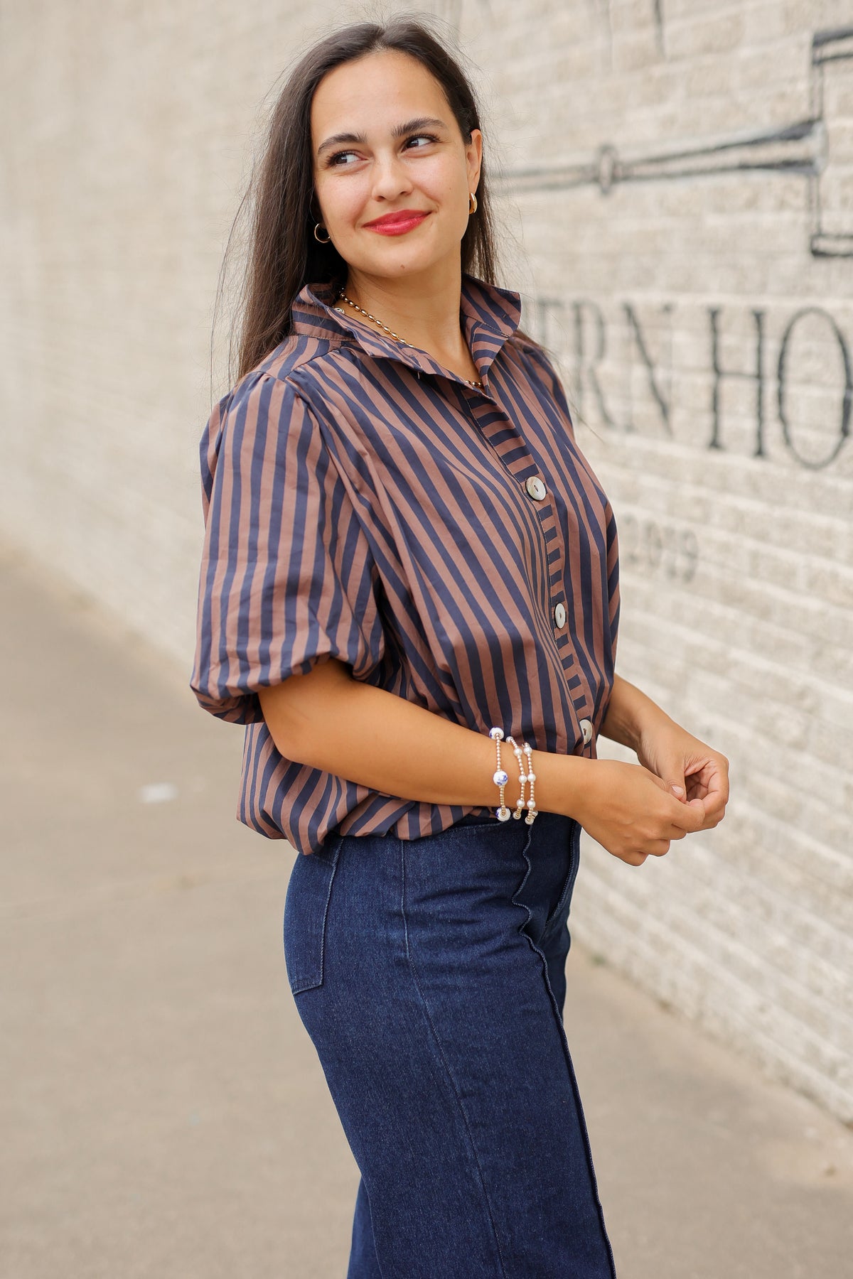 Brunette model wearing a navy and brown stripped bubble top and dark denim jeans outside. Southern House Clothing