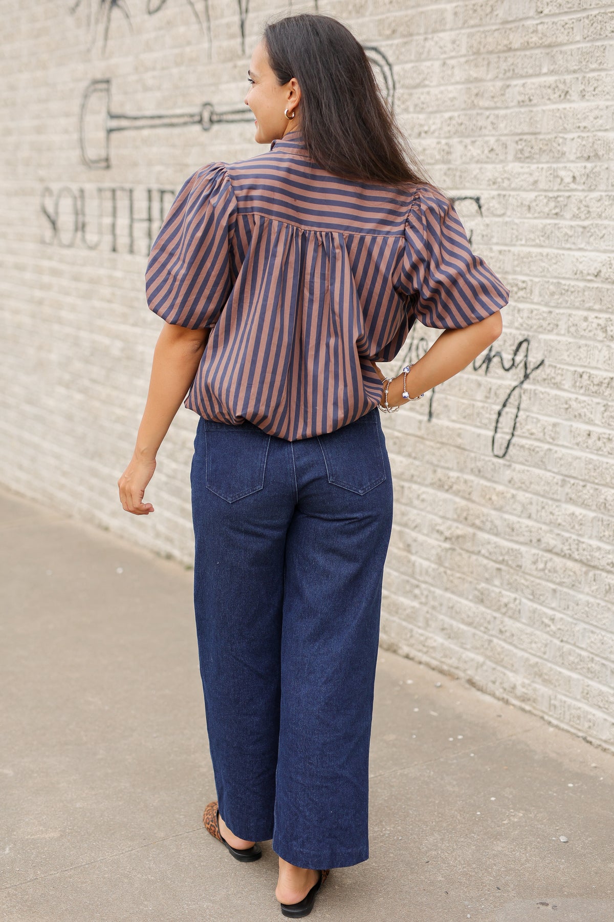 Brunette model wearing a navy and brown stripped bubble top and dark denim jeans outside. Southern House Clothing