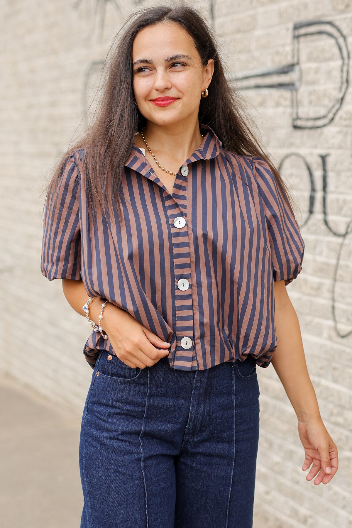 Brunette model wearing a navy and brown stripped bubble top and dark denim jeans outside. Southern House Clothing