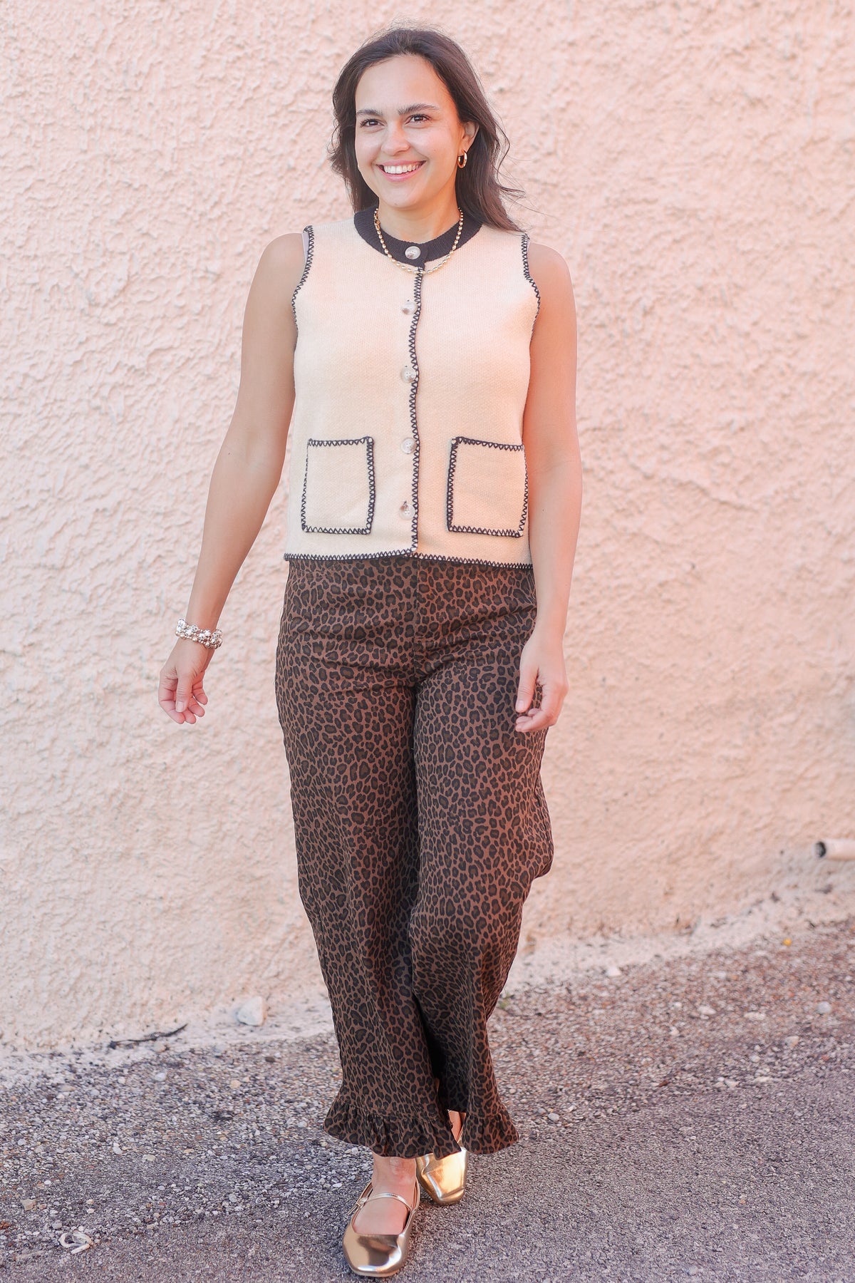 Woman wearing a patterned vest and pants against a light pink wall.