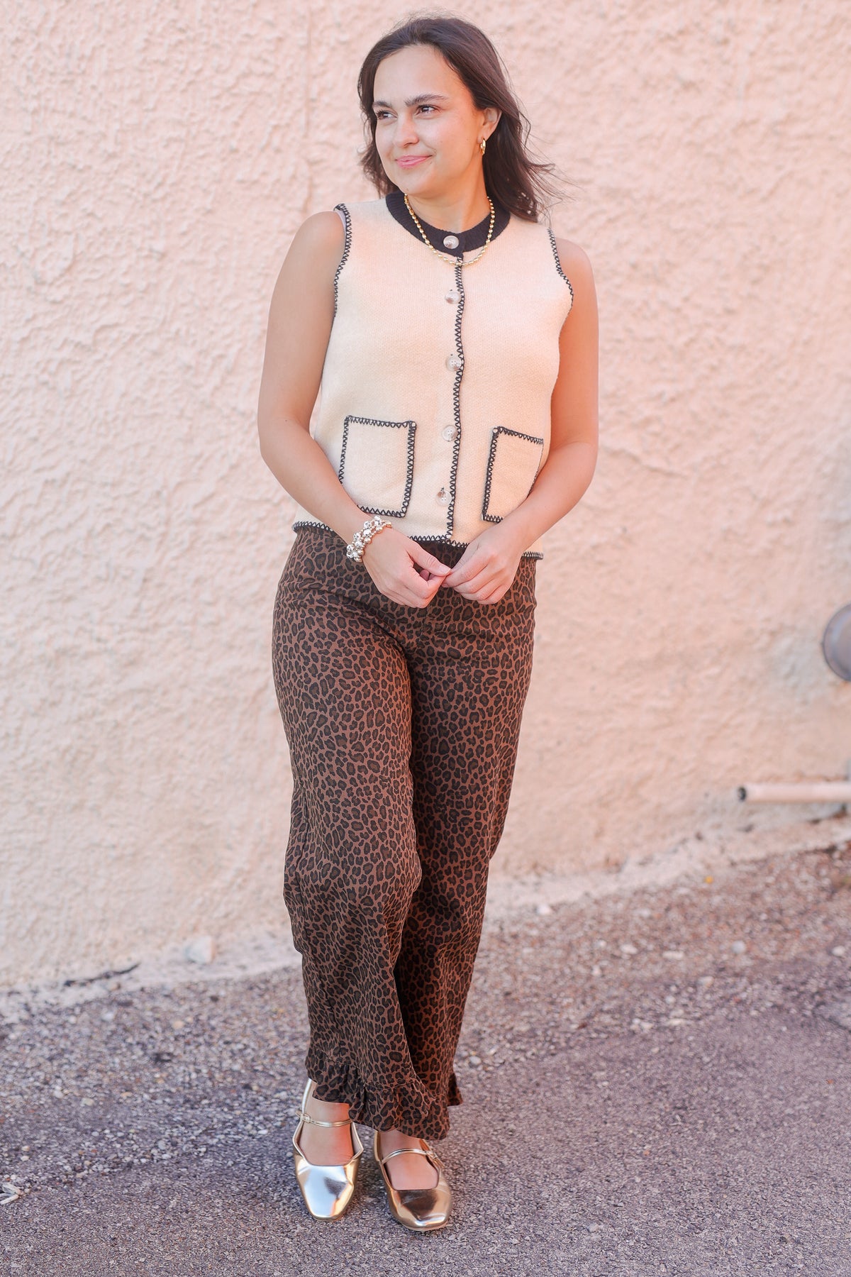 Woman wearing a sleeveless top and patterned pants standing against a textured wall.