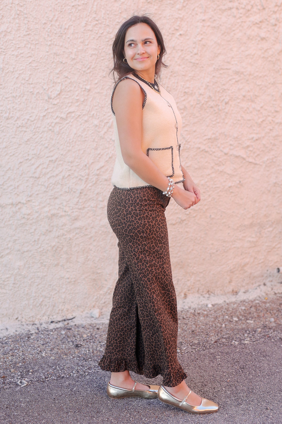 Woman wearing a beige top and patterned pants standing against a light pink wall.