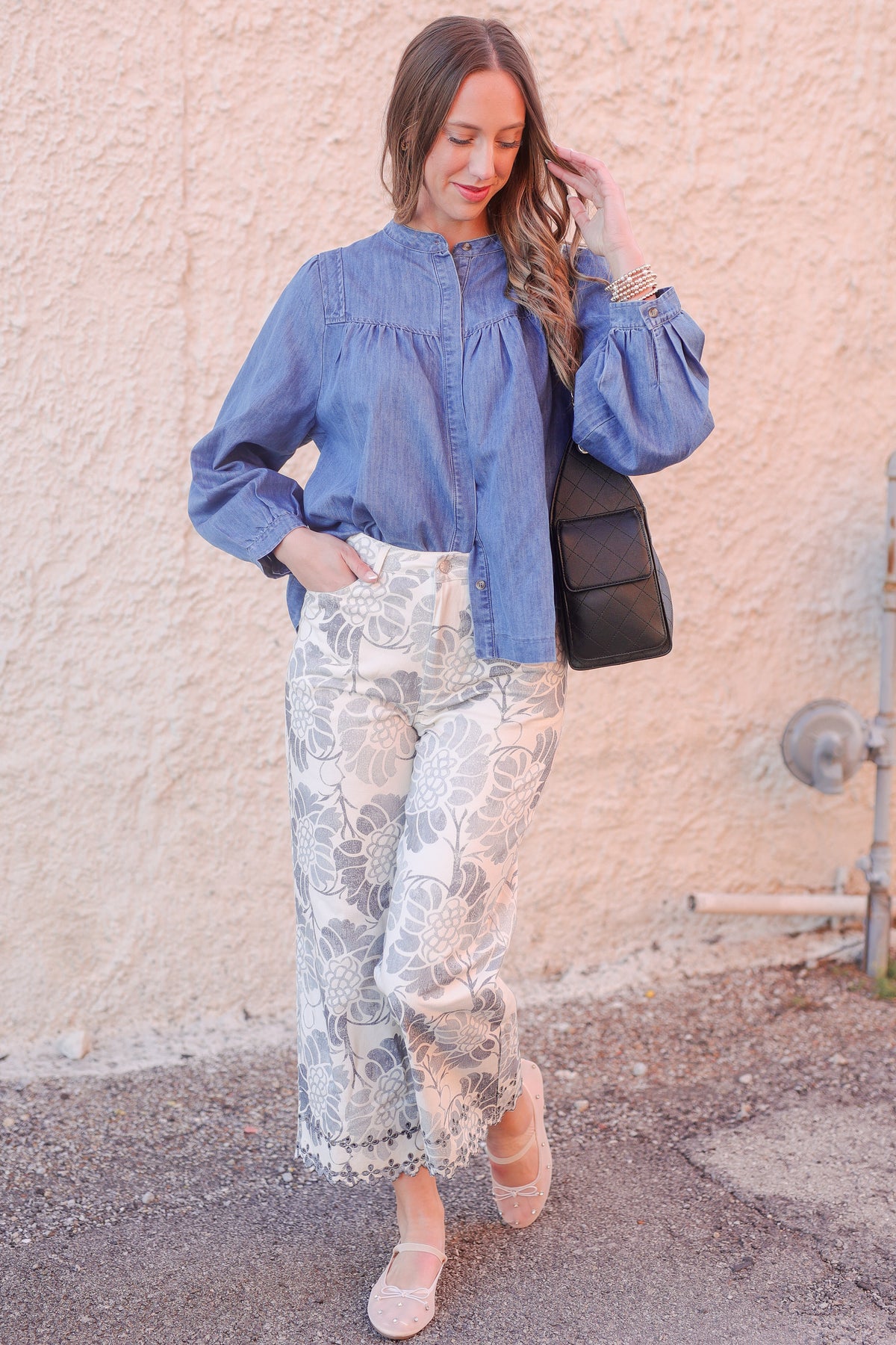 Woman wearing a blue denim shirt and patterned pants against a beige wall.