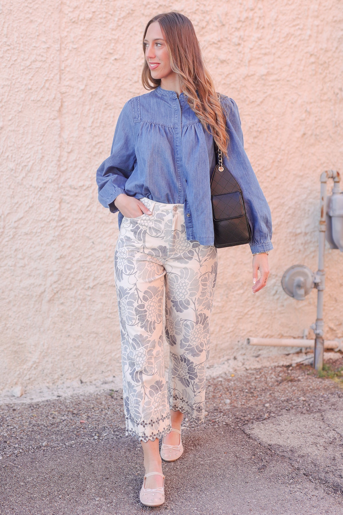 Woman wearing a blue denim shirt and floral pants against a beige wall.