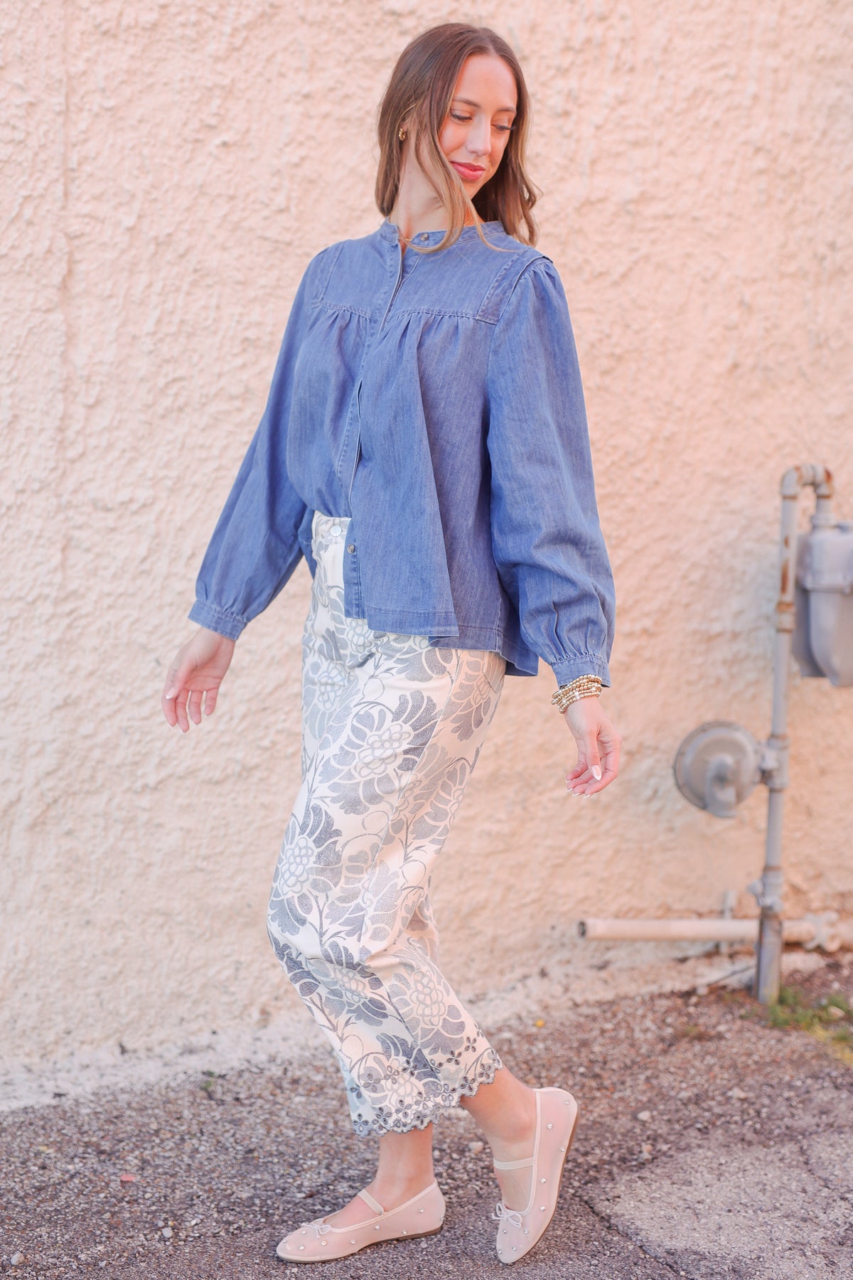 Woman wearing a blue blouse and patterned pants against a textured wall.