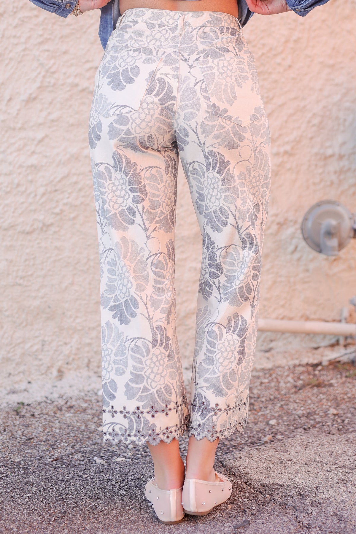 Person wearing floral-patterned pants standing against a textured wall.