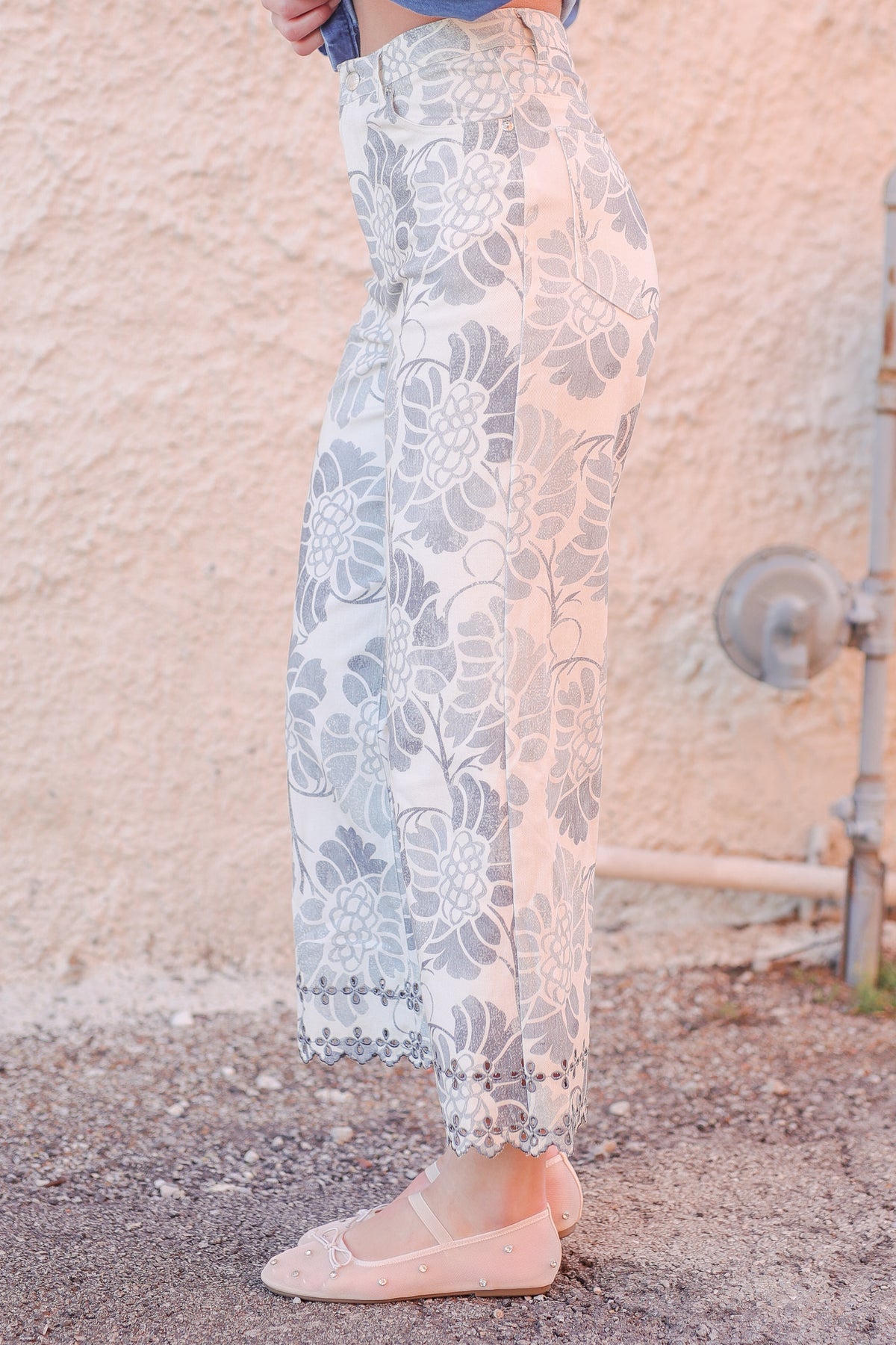 Person wearing light-colored lace pants standing against a textured wall.