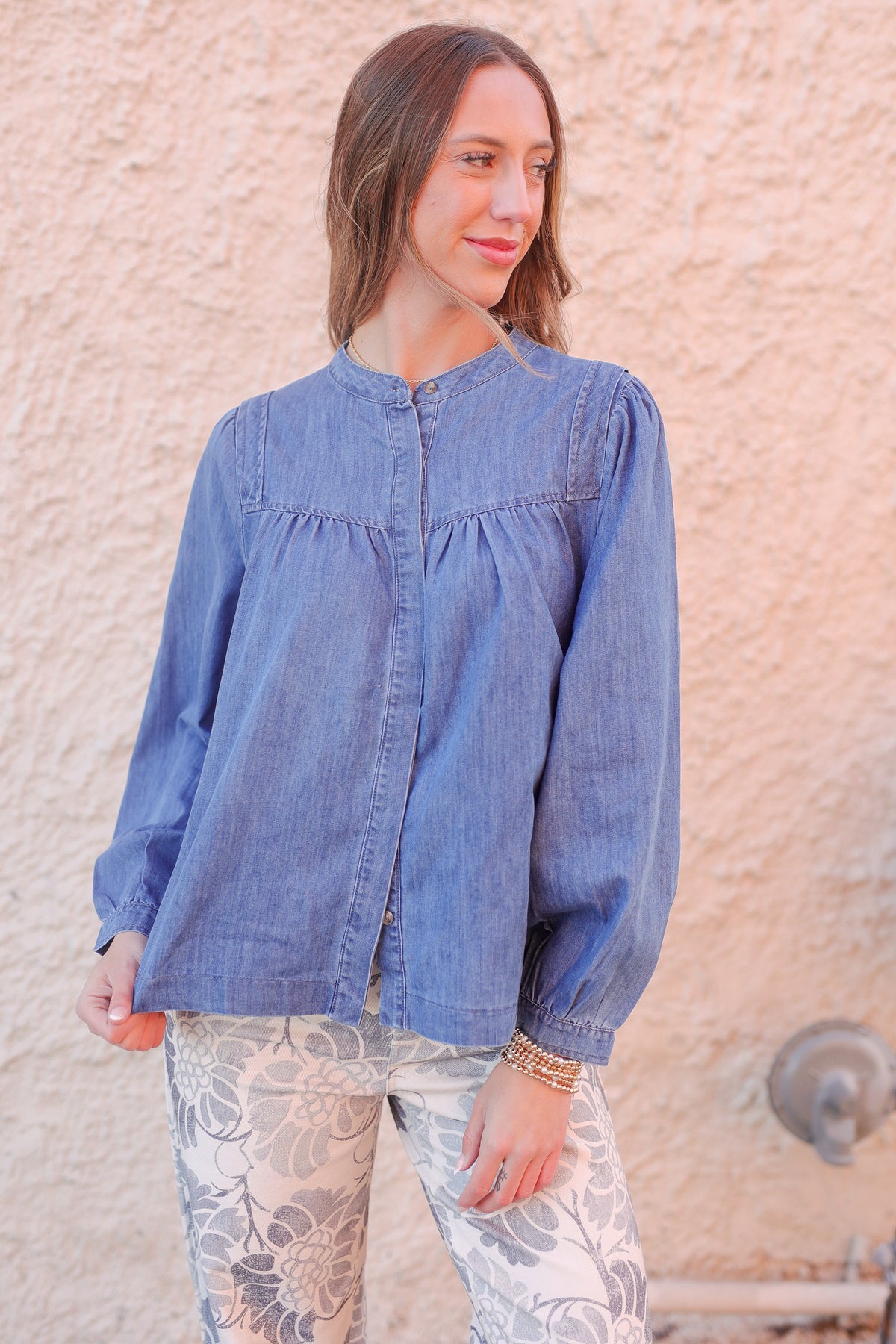 Woman wearing a blue denim shirt against a textured wall.