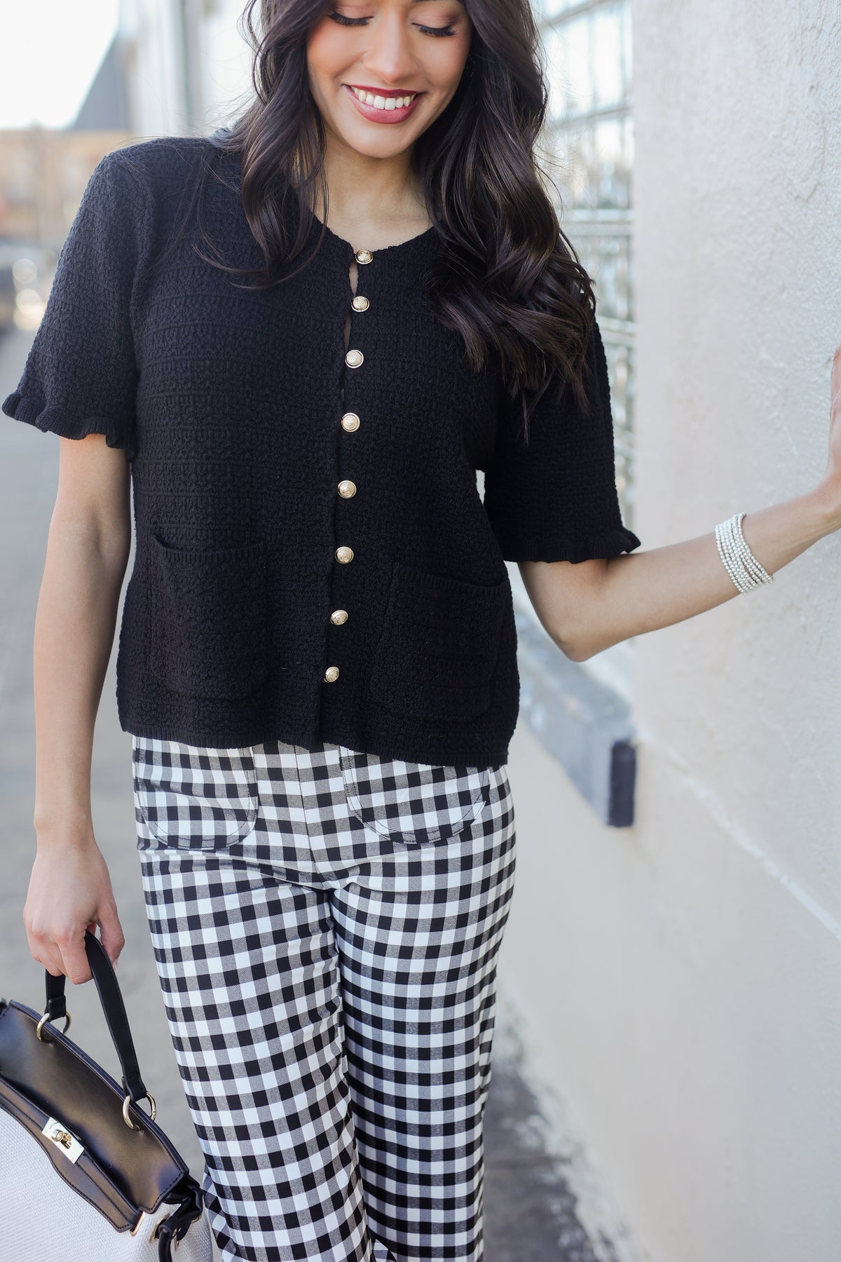 Woman wearing a black cardigan with white buttons and gingham pants, standing outdoors.