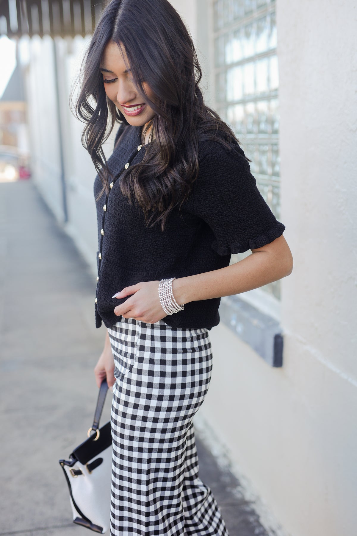Woman wearing a black jacket and gingham pants outdoors.