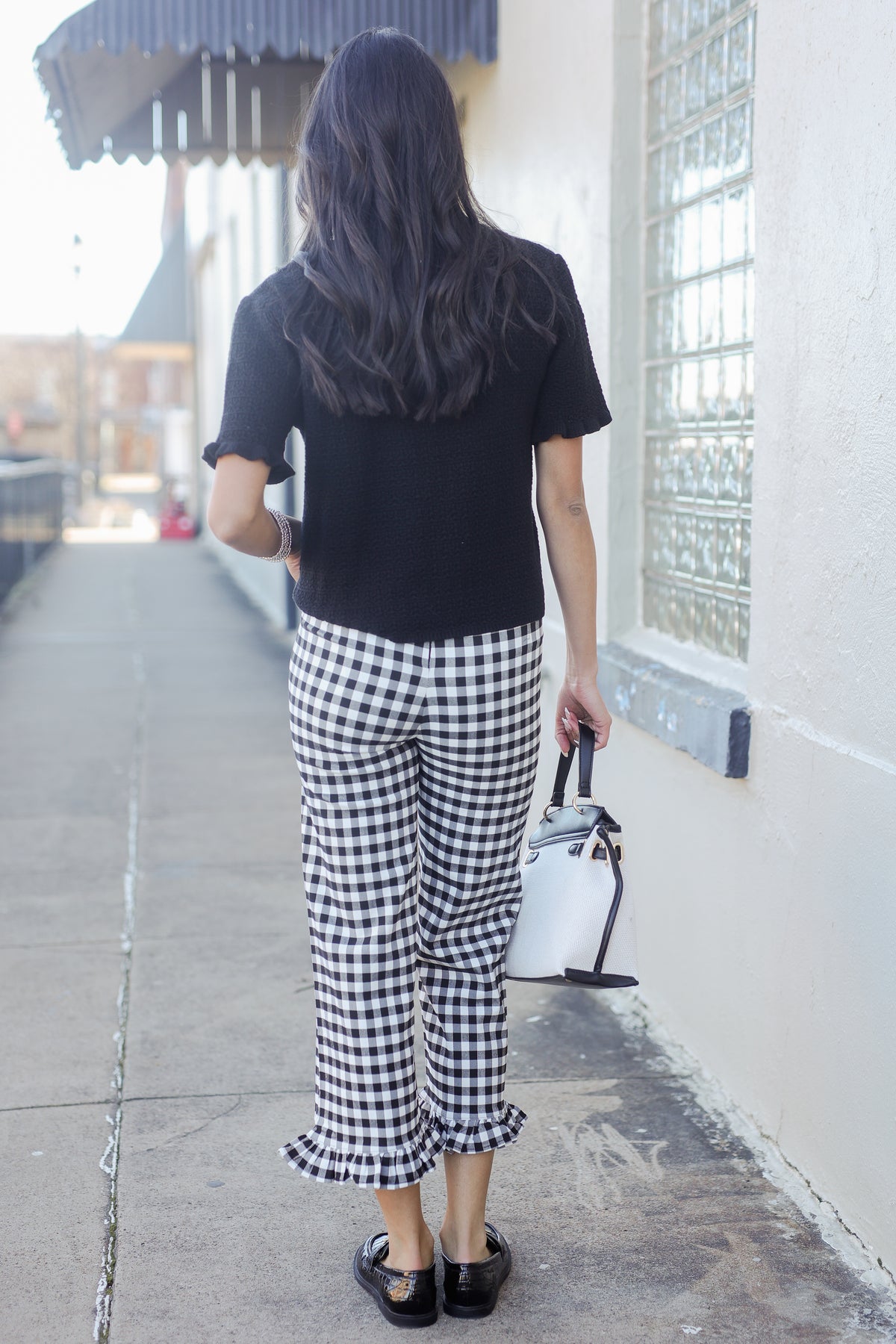 Person wearing a black t-shirt and gingham pants walking on a sidewalk.