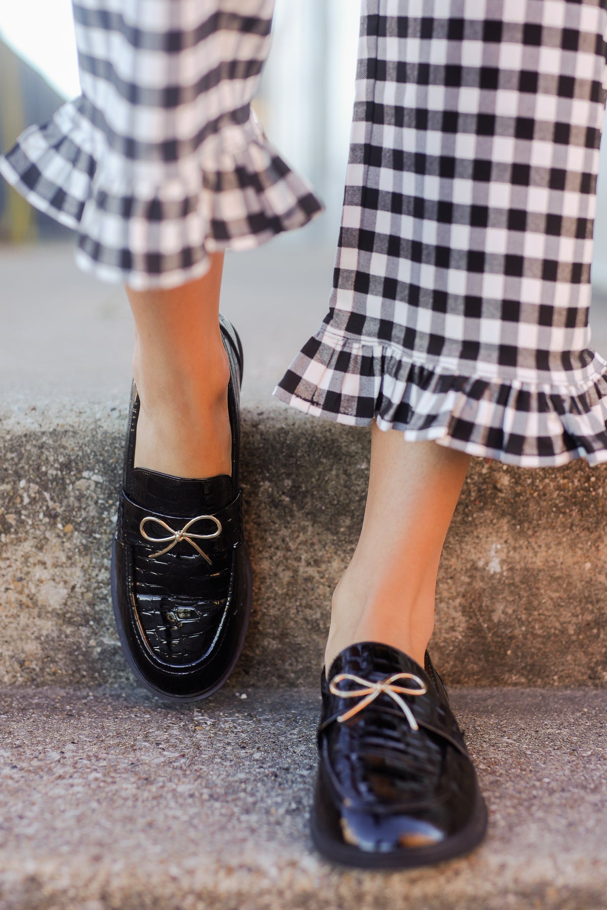 Black loafers worn with a checkered dress on a stone surface