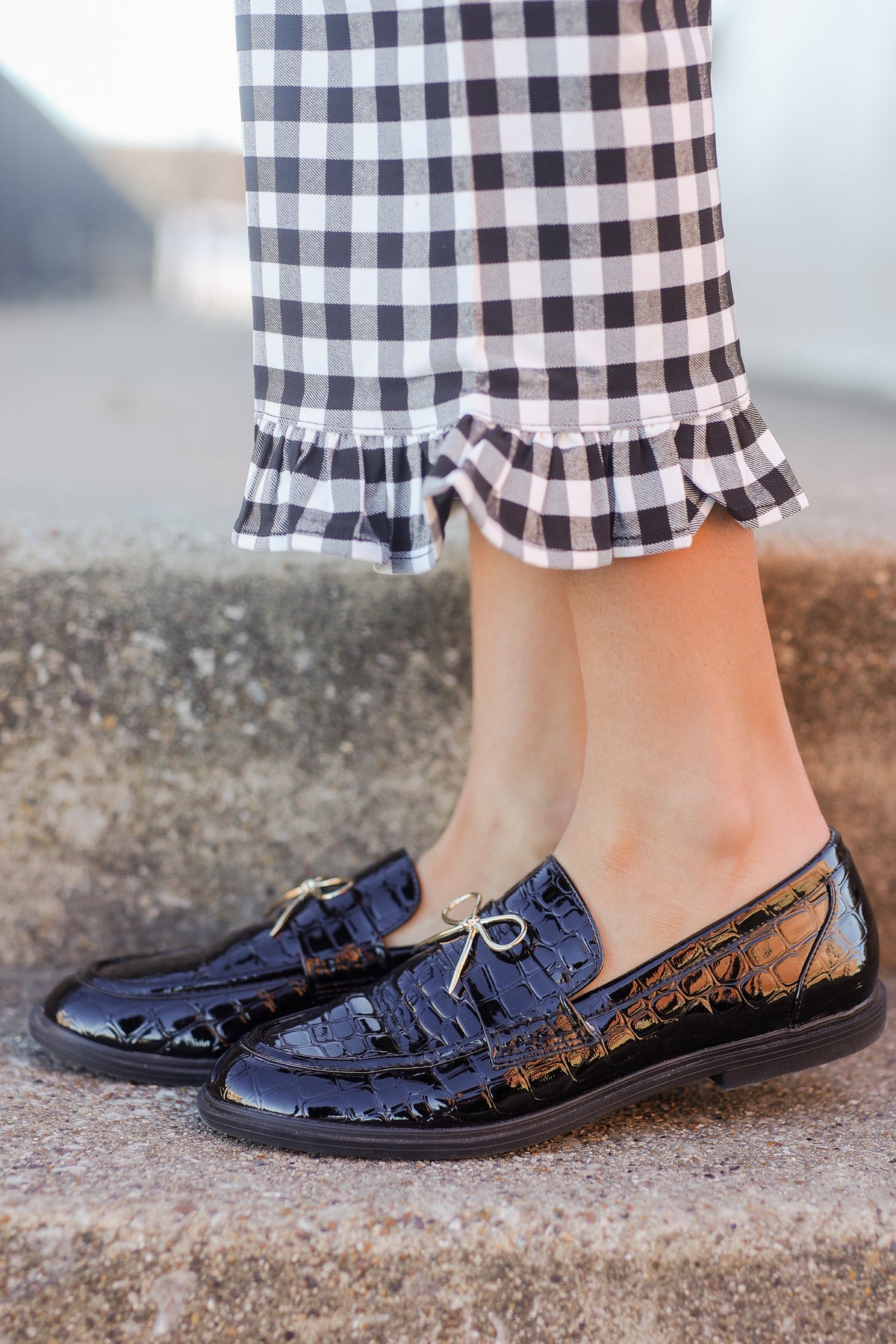 Navy blue patent leather shoes worn with a checkered skirt on a blurred outdoor background