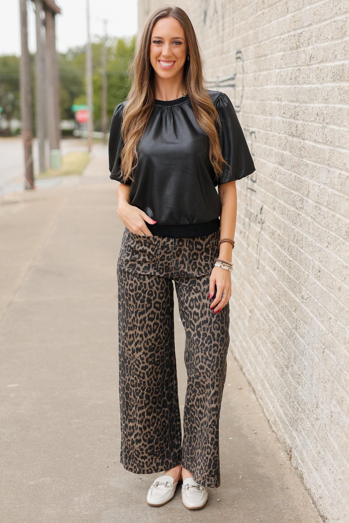 Blonde model standing outside wearing a black blouse and leopard denim pants with white slides. | Southern House Clothing|
