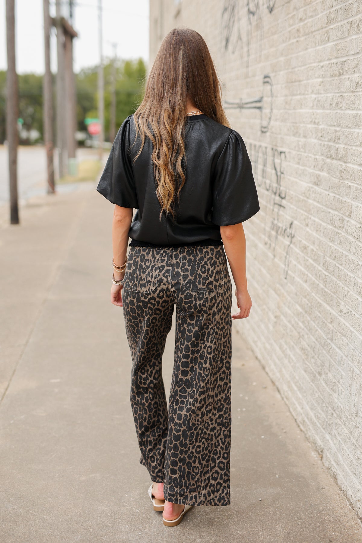Blonde model standing outside wearing a black blouse and leopard denim pants with white slides. | Southern House Clothing|