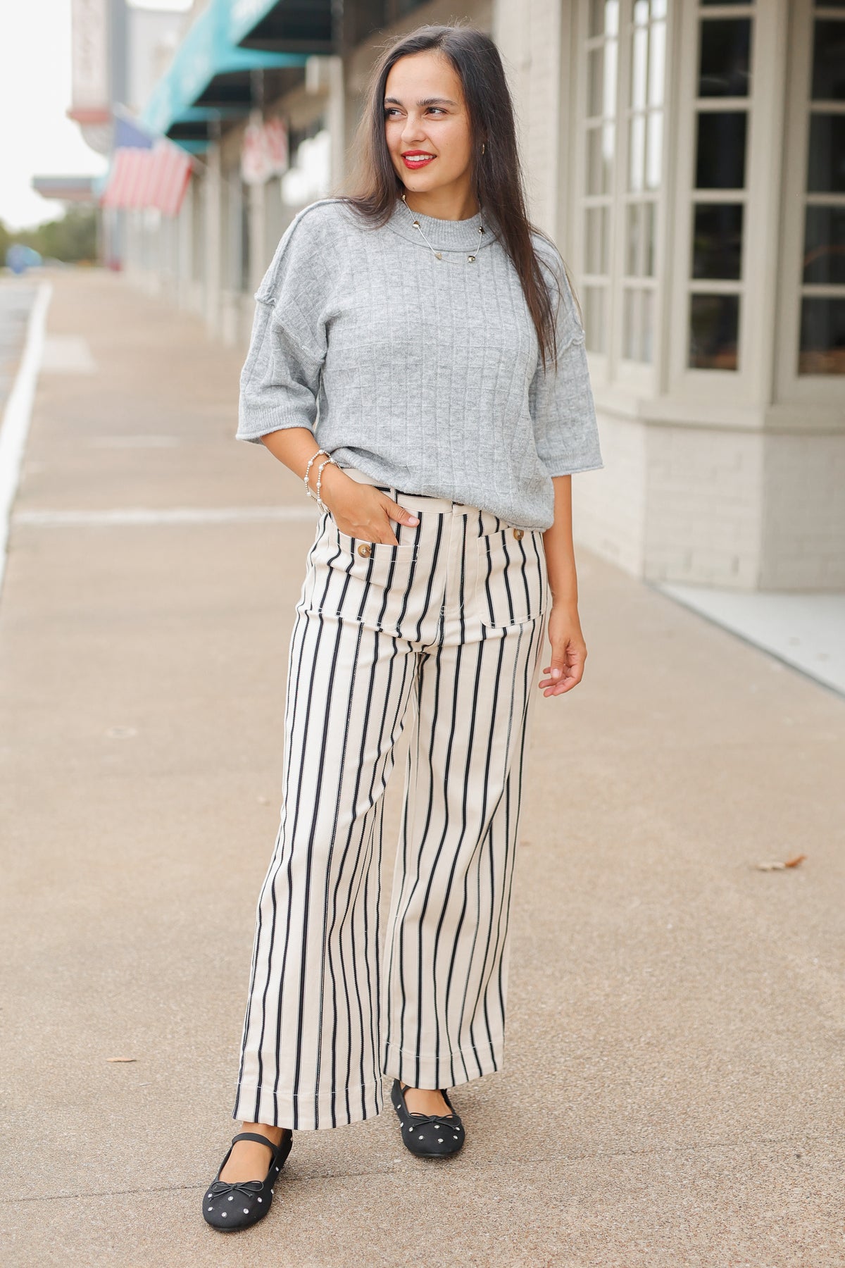 Brunette model wearing the Whitlock Grid Knit Top in Heather Gray featuring a textured grid pattern, round neckline, dropped shoulders, and elbow-length sleeves, styled with cream and black striped wide-leg pants called the Bristols. Southern House Clothing.
