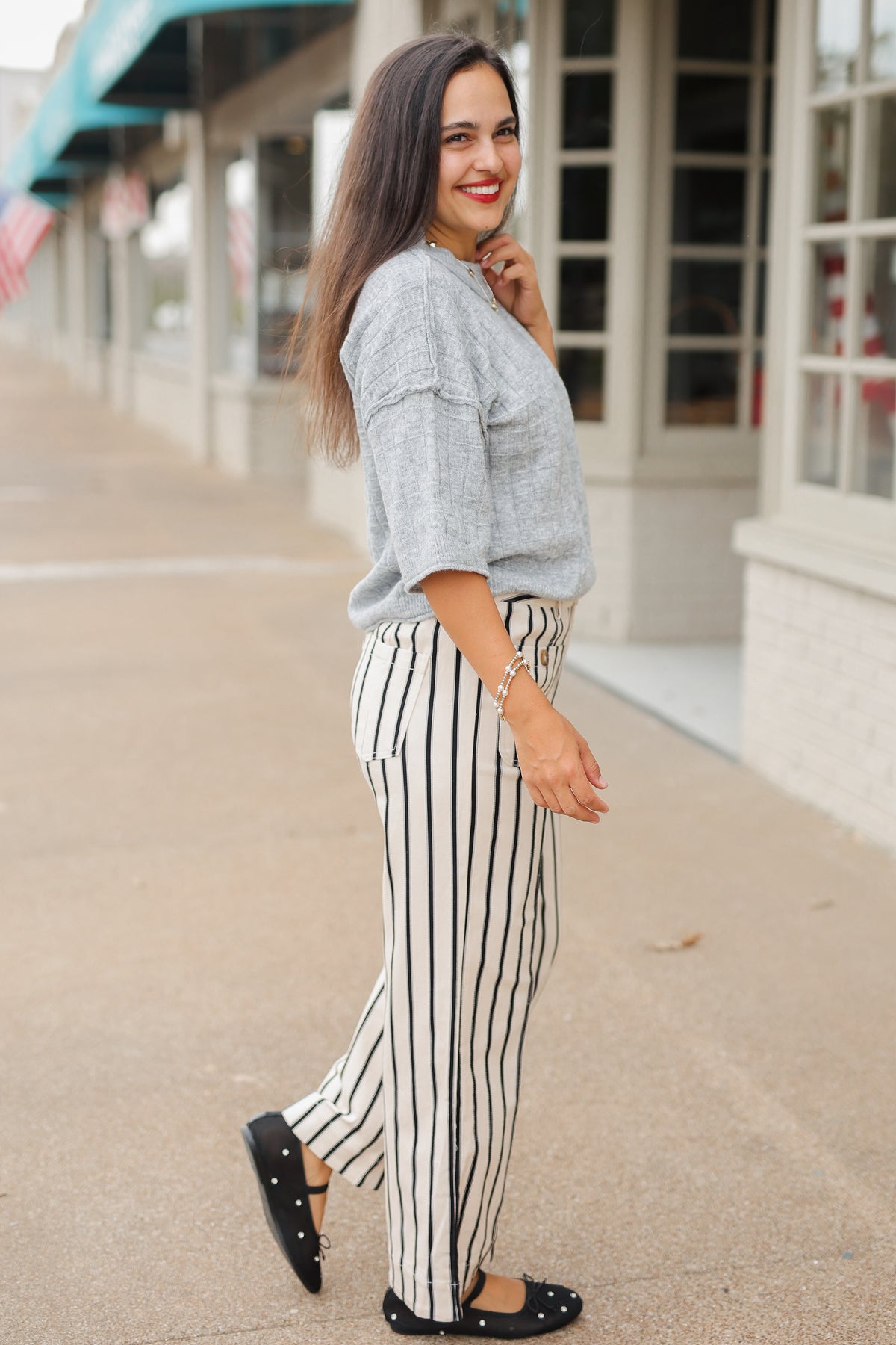 Brunette model wearing the Whitlock Grid Knit Top in Heather Gray featuring a textured grid pattern, round neckline, dropped shoulders, and elbow-length sleeves, styled with cream and black striped wide-leg pants called the Bristols. Southern House Clothing.