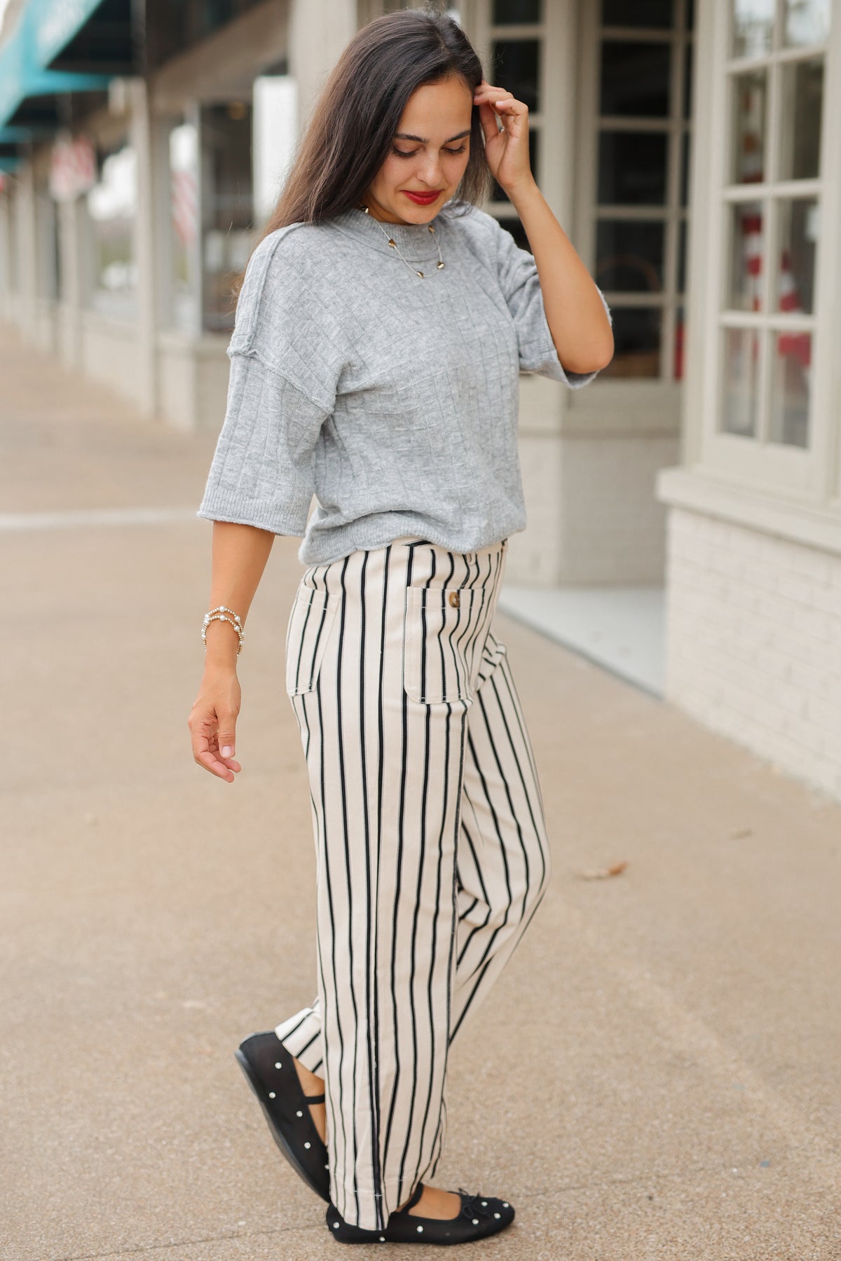 Brunette model wearing the Whitlock Grid Knit Top in Heather Gray featuring a textured grid pattern, round neckline, dropped shoulders, and elbow-length sleeves, styled with cream and black striped wide-leg pants called the Bristols. Southern House Clothing.