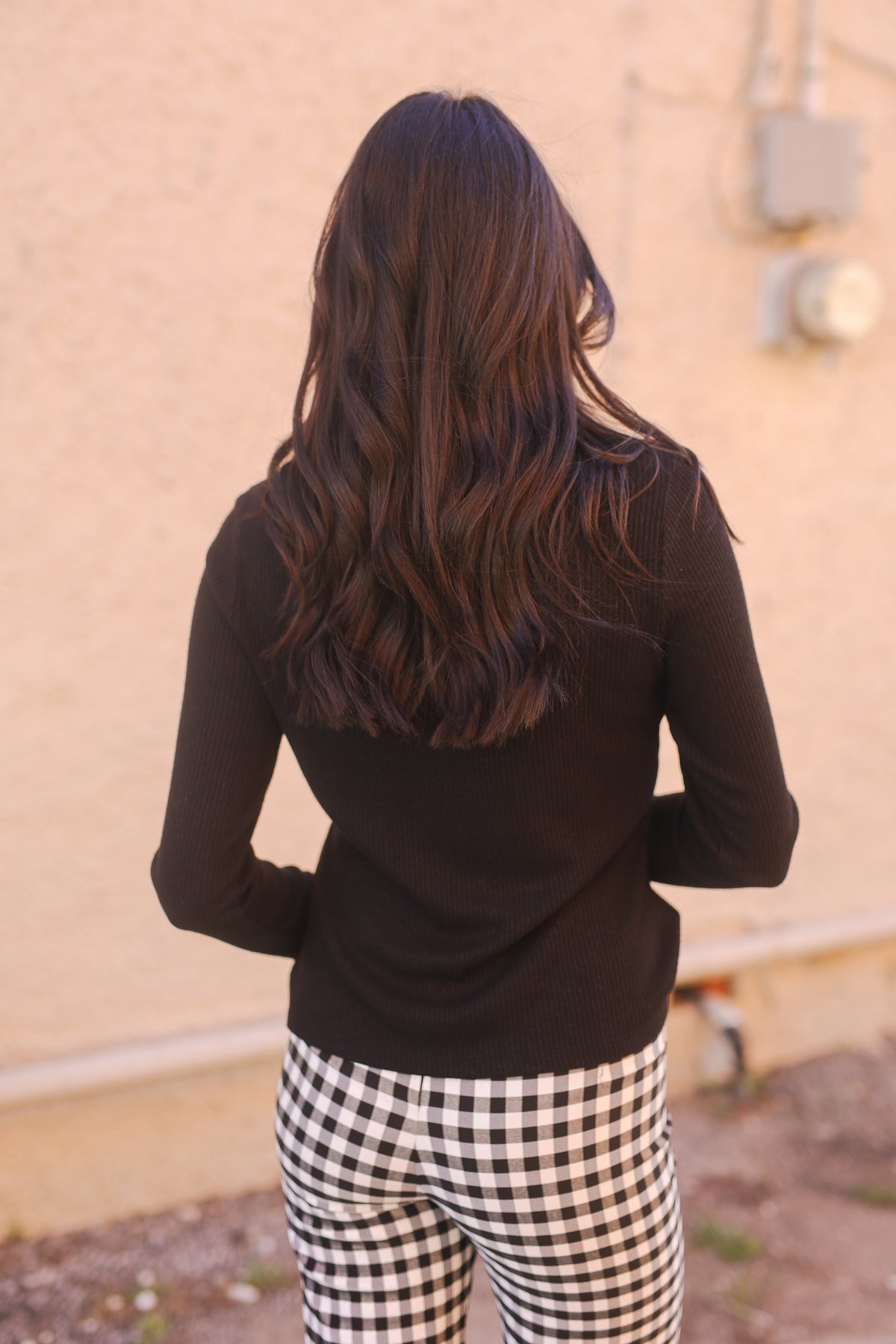 Woman outside wearing a black top and gingham pants.