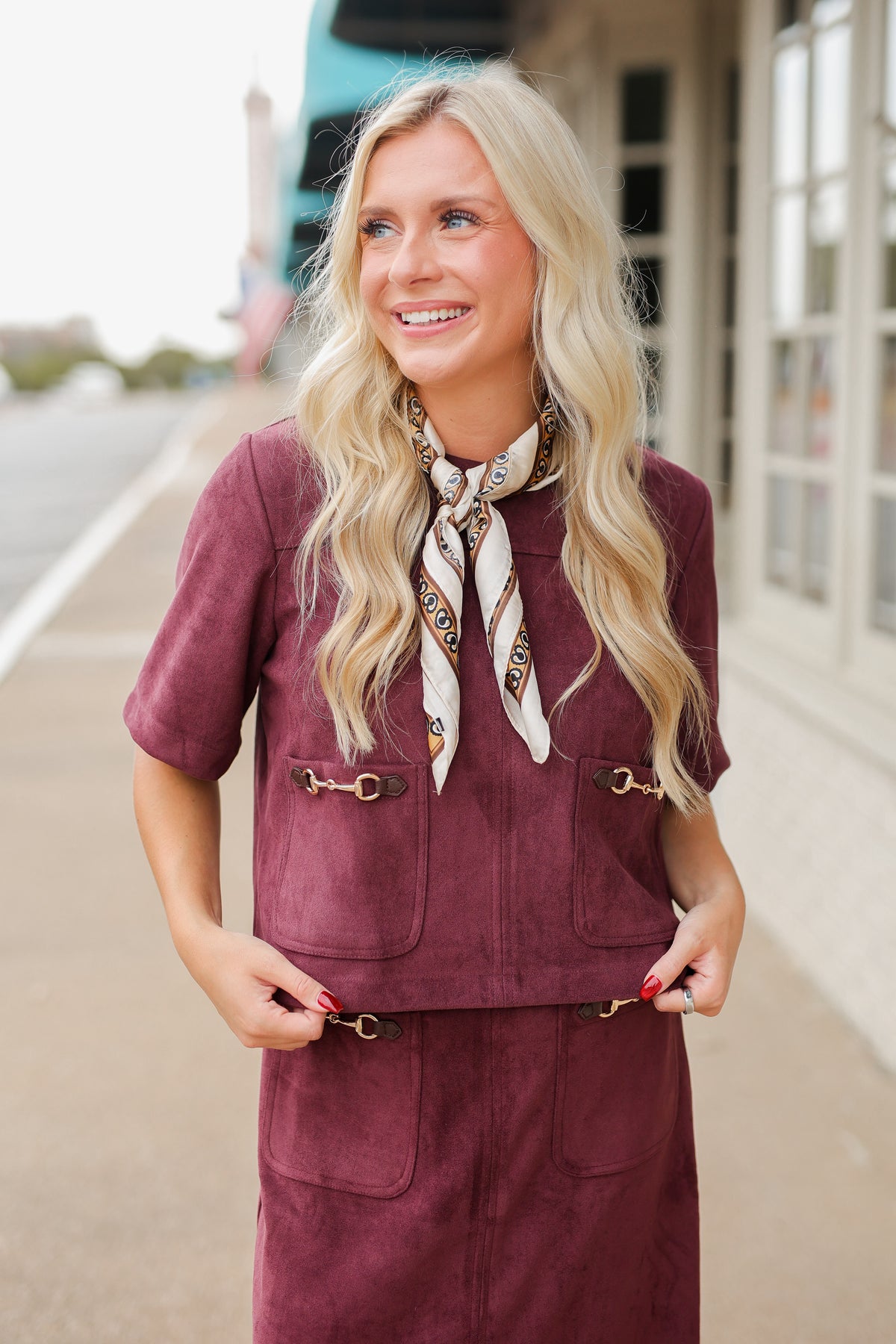 Blonde model wearing a burgundy colored satin top with a matching skirt to make it a set standing outside with brown boots. Southern House Clothing