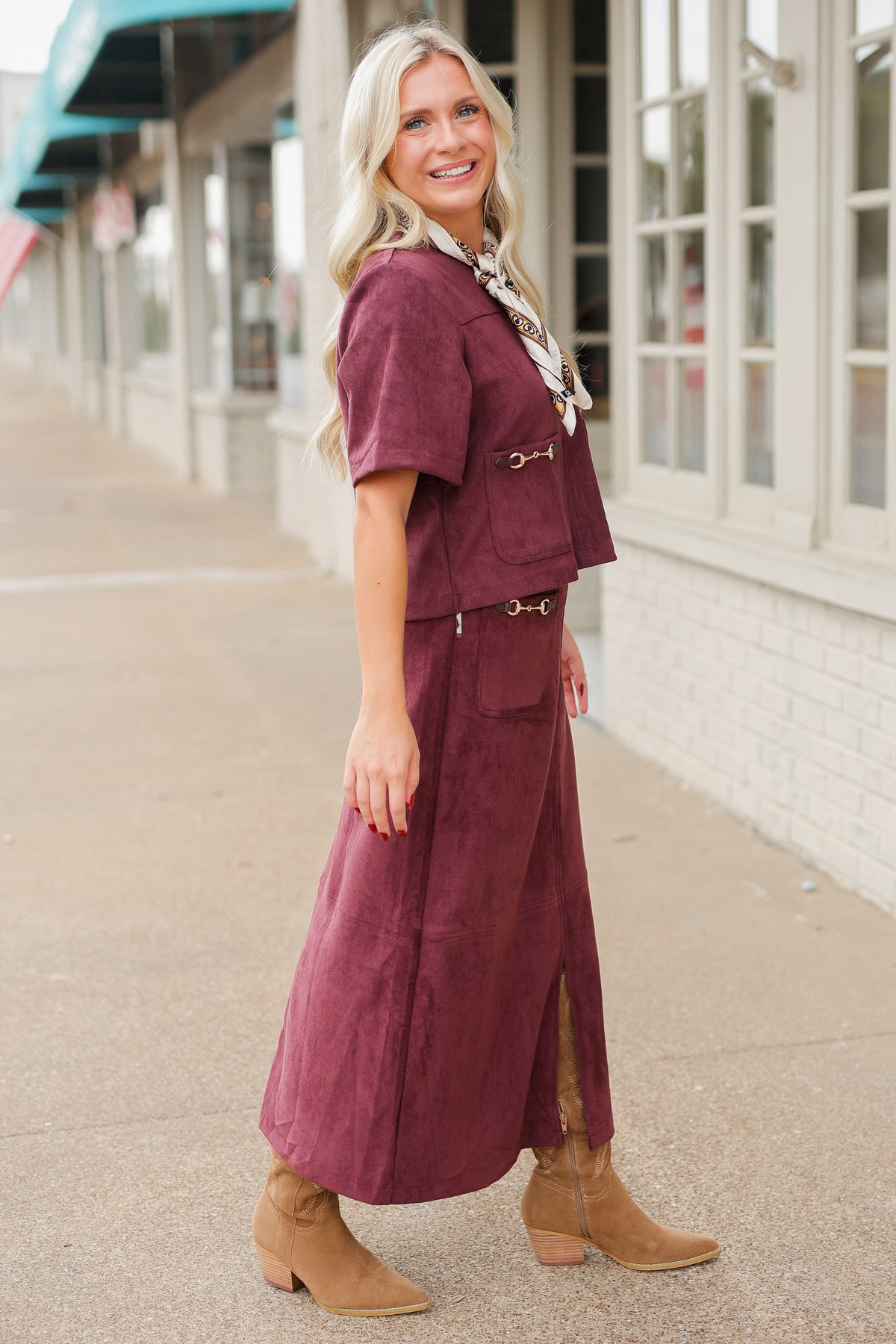 Blonde model wearing a burgundy colored satin top with a matching skirt to make it a set standing outside with brown boots. Southern House Clothing