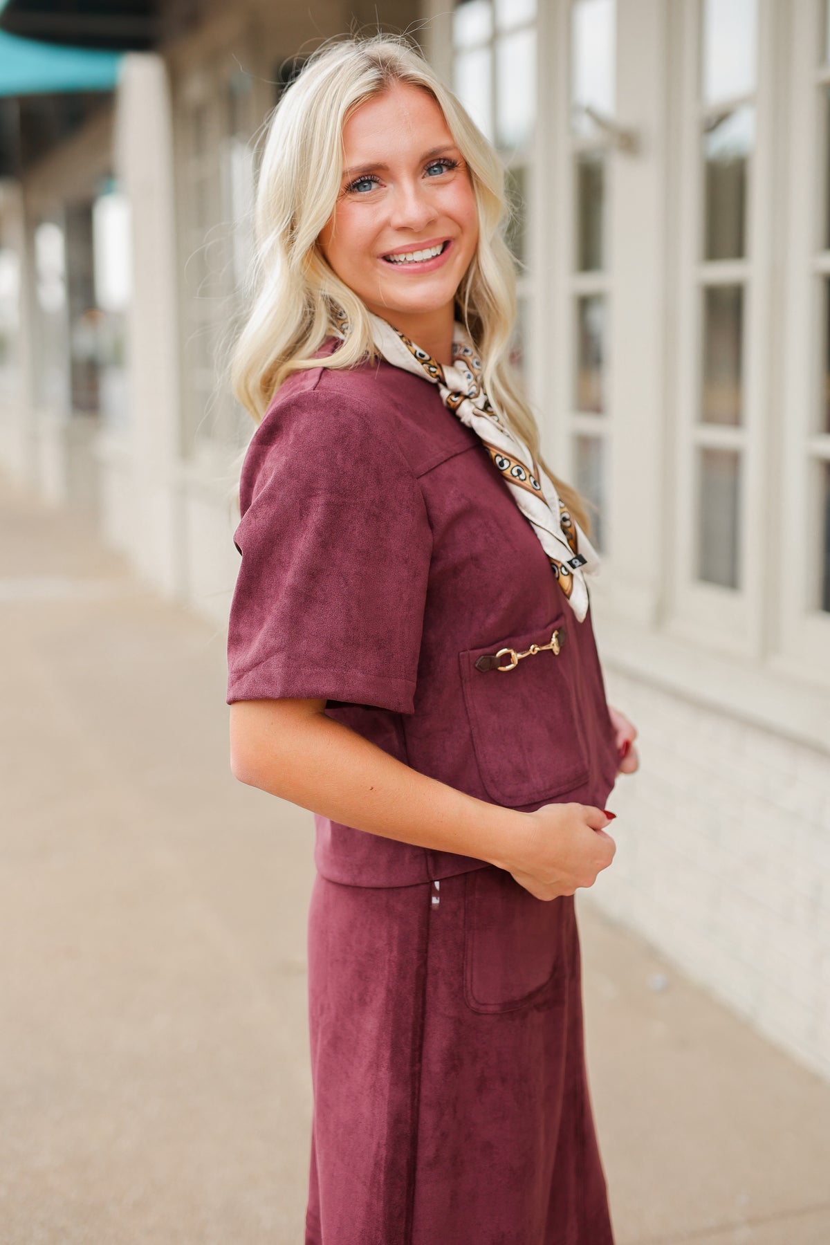 Blonde model wearing a burgundy colored satin top with a matching skirt to make it a set standing outside with brown boots. Southern House Clothing