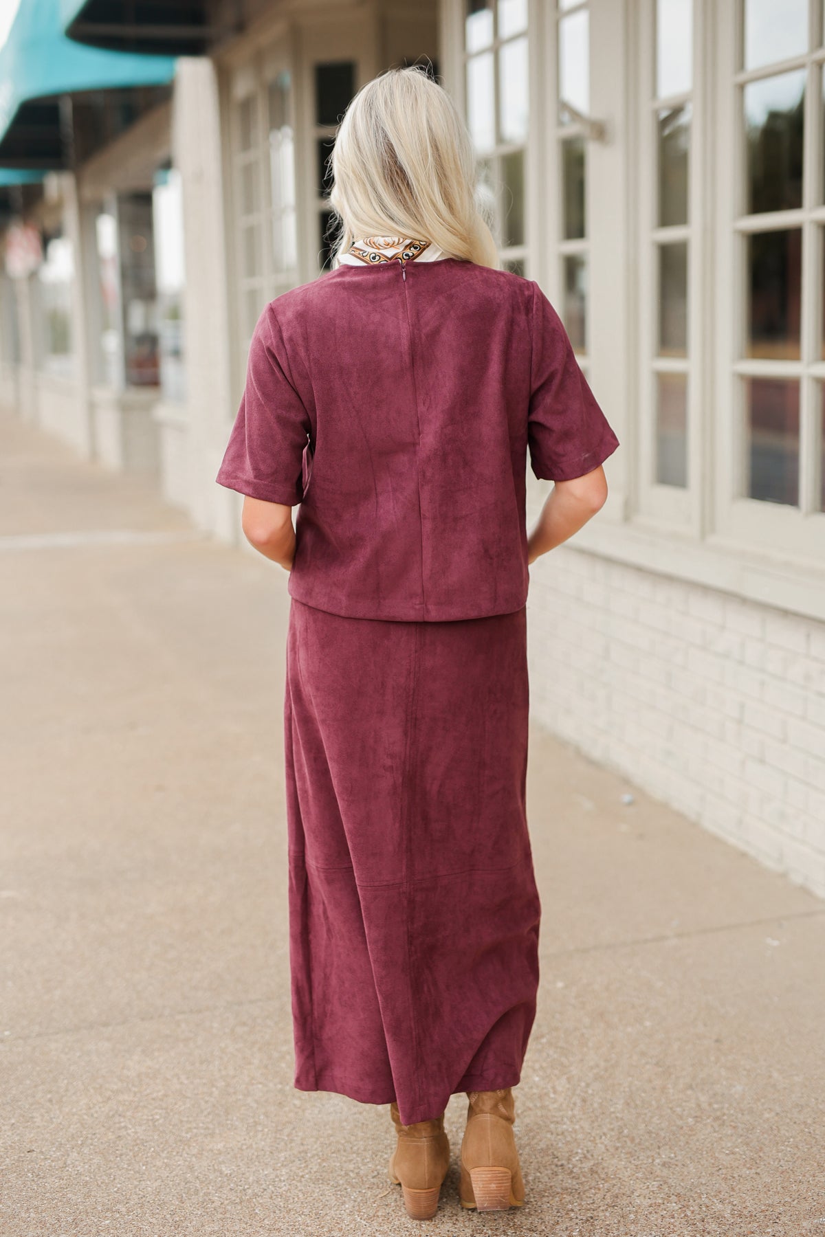 Blonde model wearing a burgundy colored satin top with a matching skirt to make it a set standing outside with brown boots. Southern House Clothing