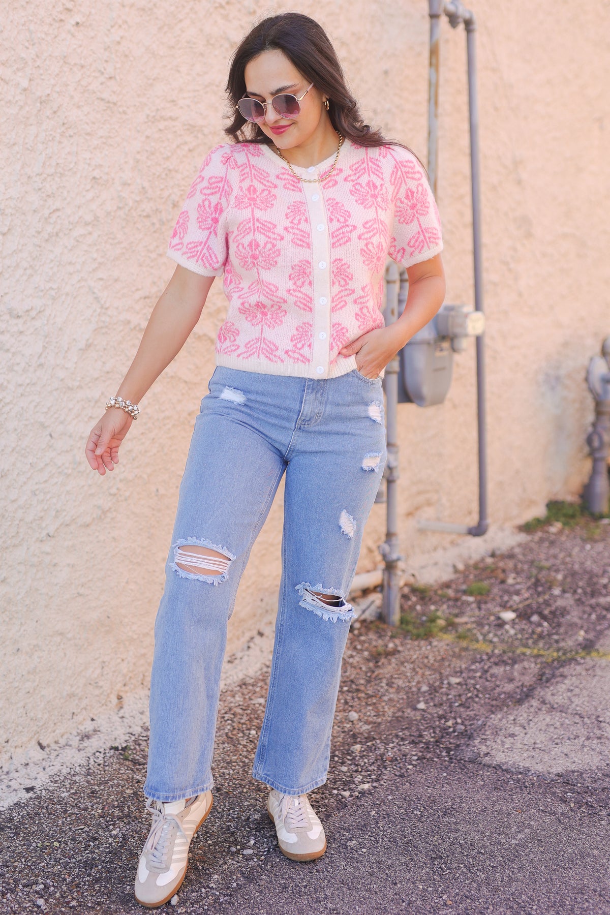 Woman wearing a pink floral blouse and blue jeans standing against a textured wall.