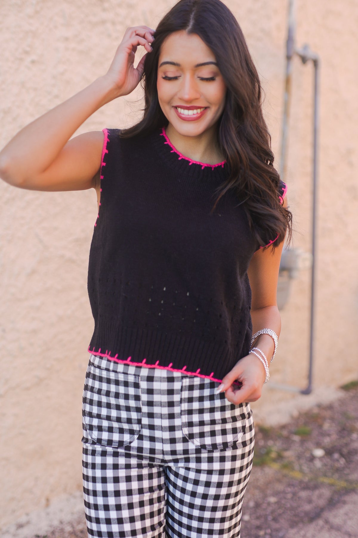 Woman wearing a black sleeveless top with pink trim and checkered pants against a beige wall.