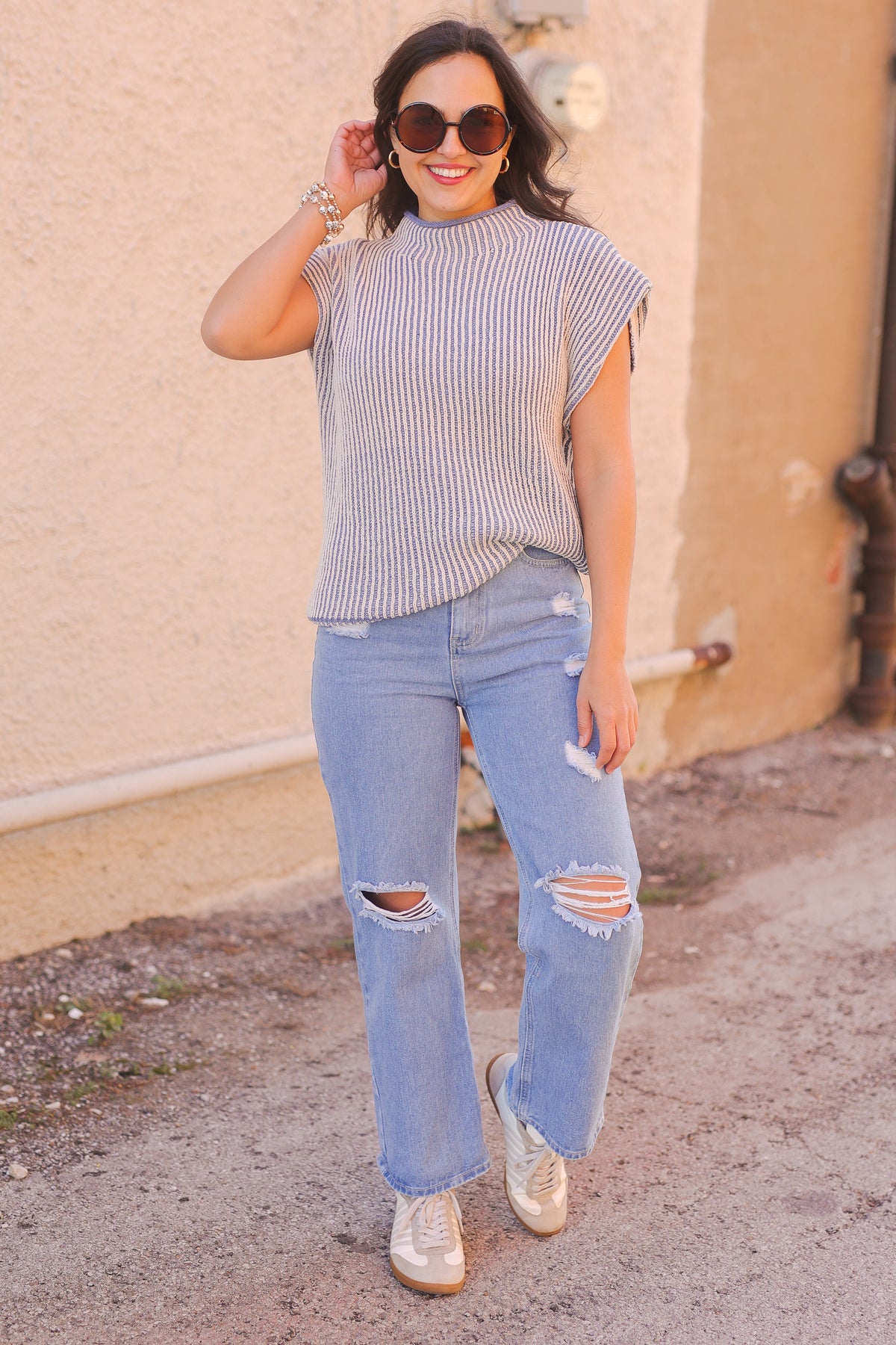 Woman wearing a striped shirt and ripped jeans standing against a beige wall.