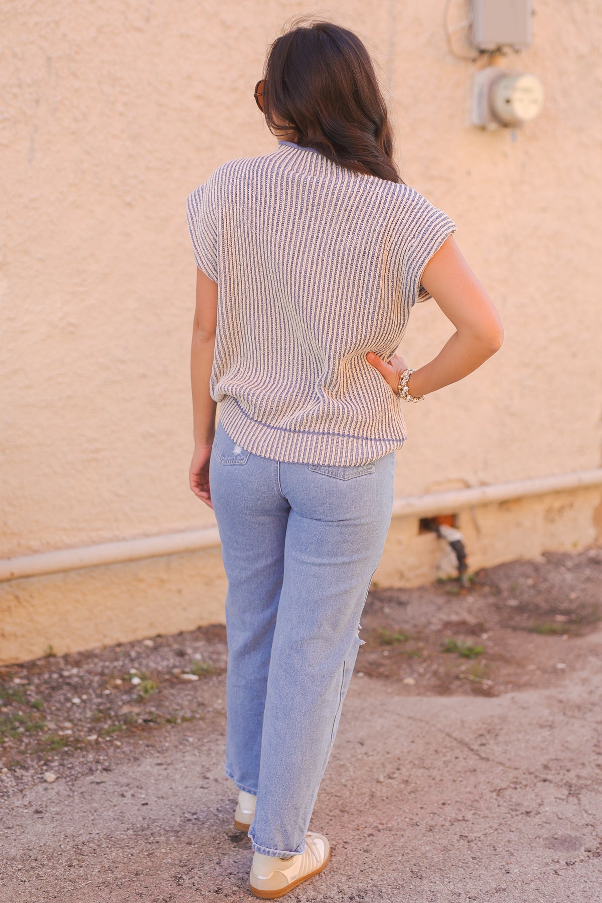 Person wearing a striped shirt and light blue jeans against a beige wall.