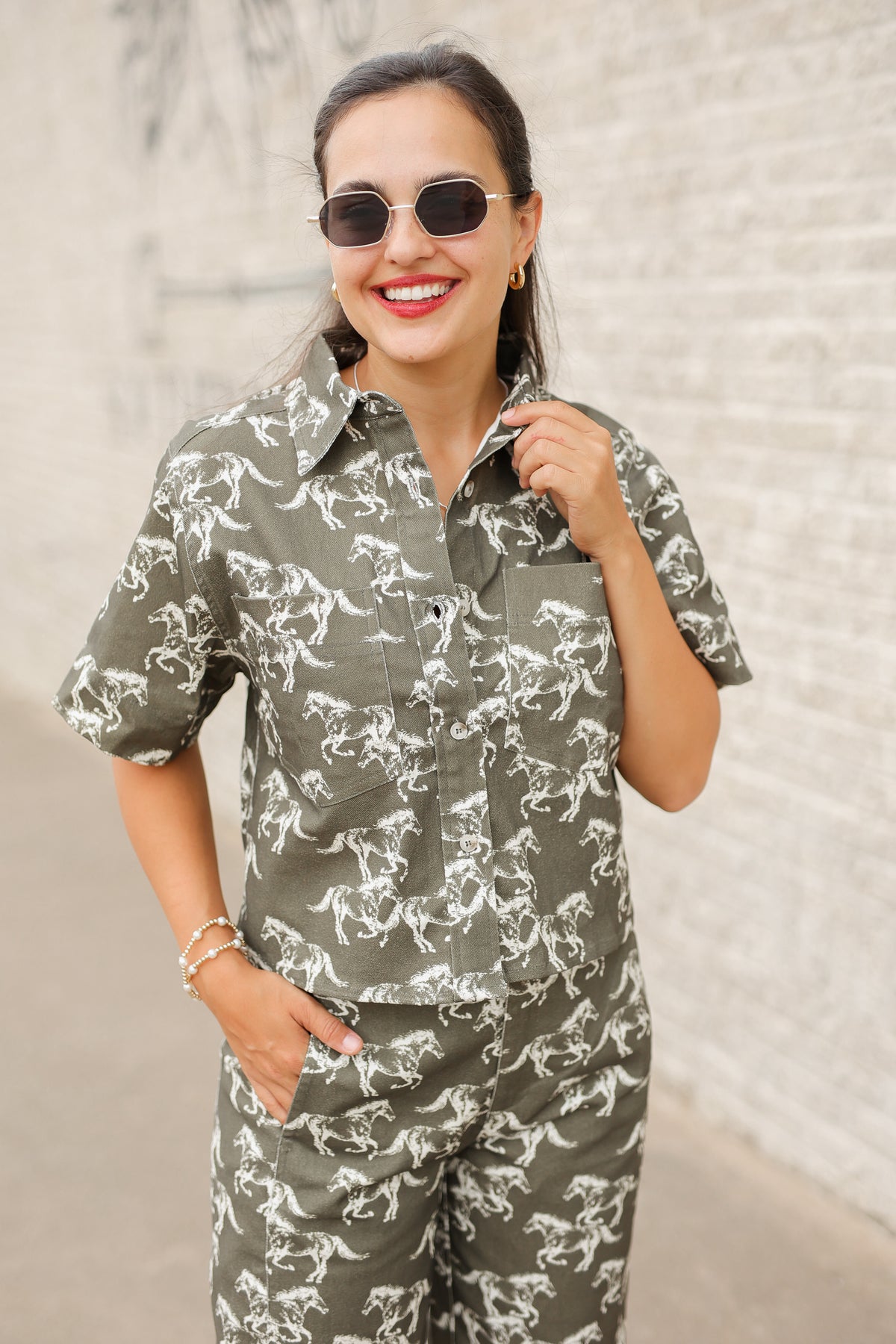 Brunette model wearing an olive colored denim set with running horse detail and white slides standing outside. Southern House Clothing.