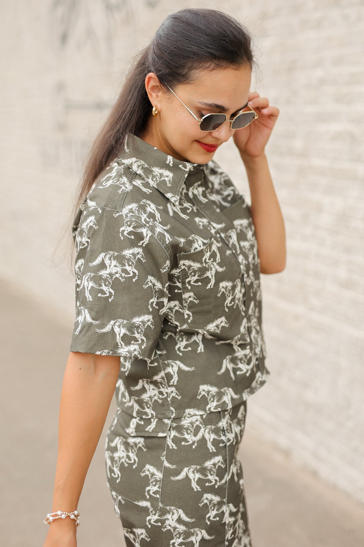 Brunette model wearing an olive colored denim set with running horse detail and white slides standing outside. Southern House Clothing.