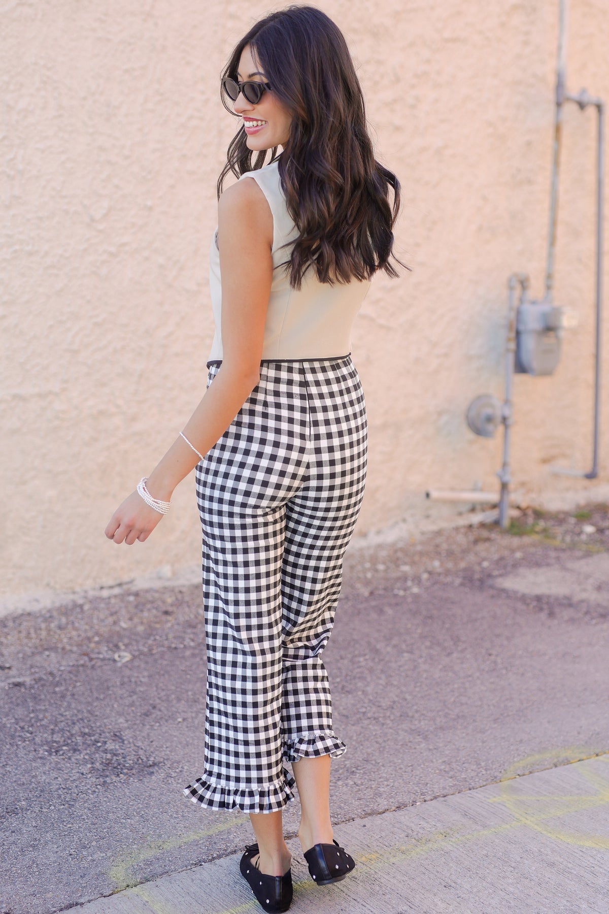 Woman wearing a sleeveless top and checkered pants standing against a beige wall.